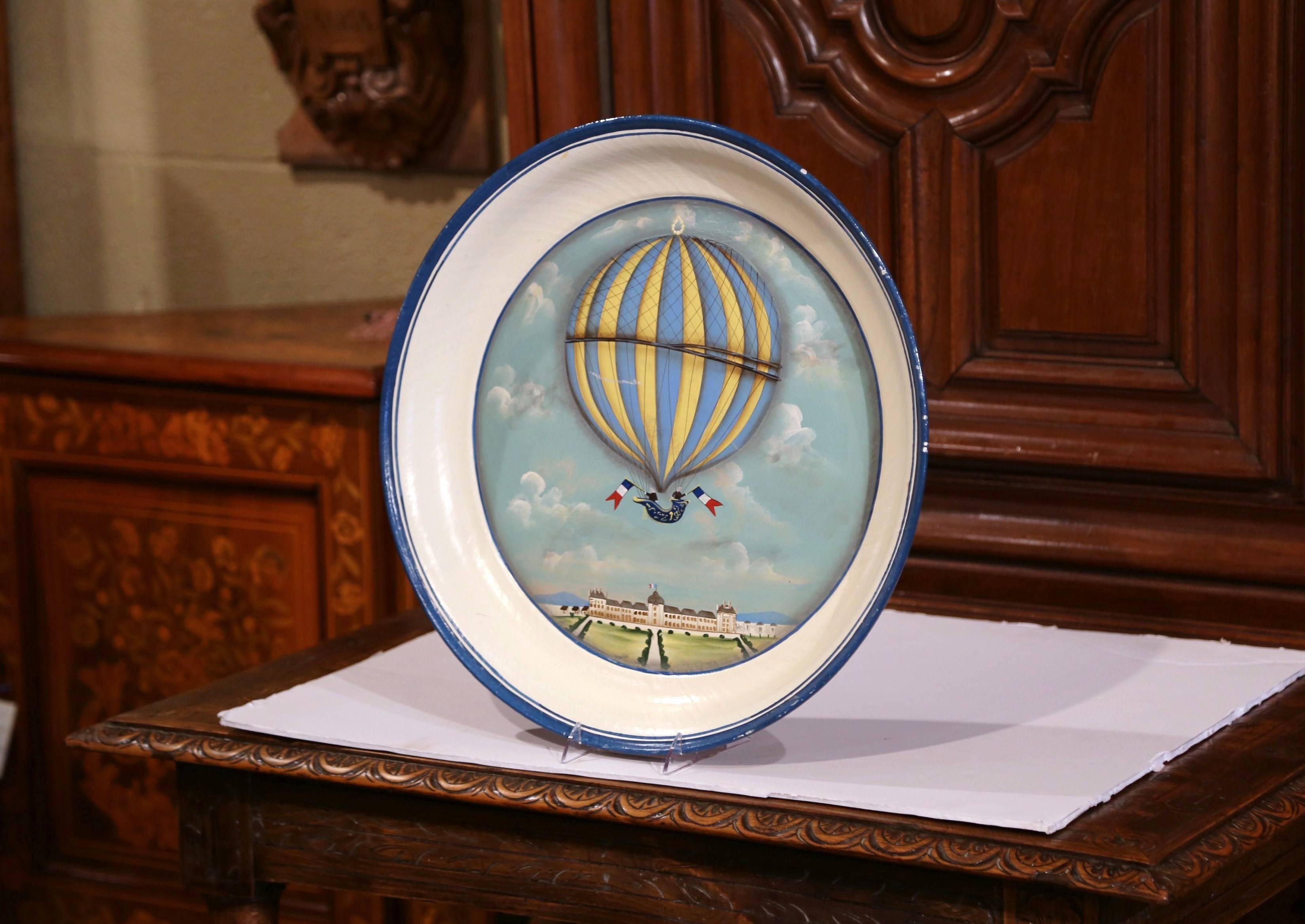 This colorful round tray was crafted in France circa 2000; the decorative piece features a blue and yellow hot air balloon flanked on both sides by the French tricolor flag and flying over a chateau in the background. Excellent condition with rich