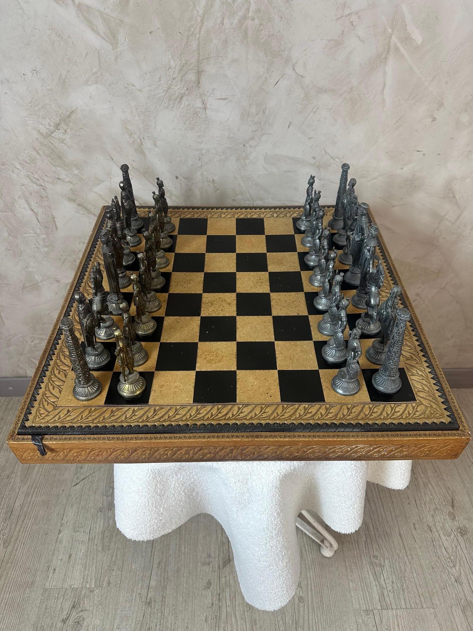 Superbo set di scacchi con scacchiera rivestita in pelle e ornata da motivi decorativi finemente lavorati. I pezzi di metallo, dorati da un lato e argentati dall'altro, presentano patine contrastanti per un look elegante e raffinato. Ogni dettaglio