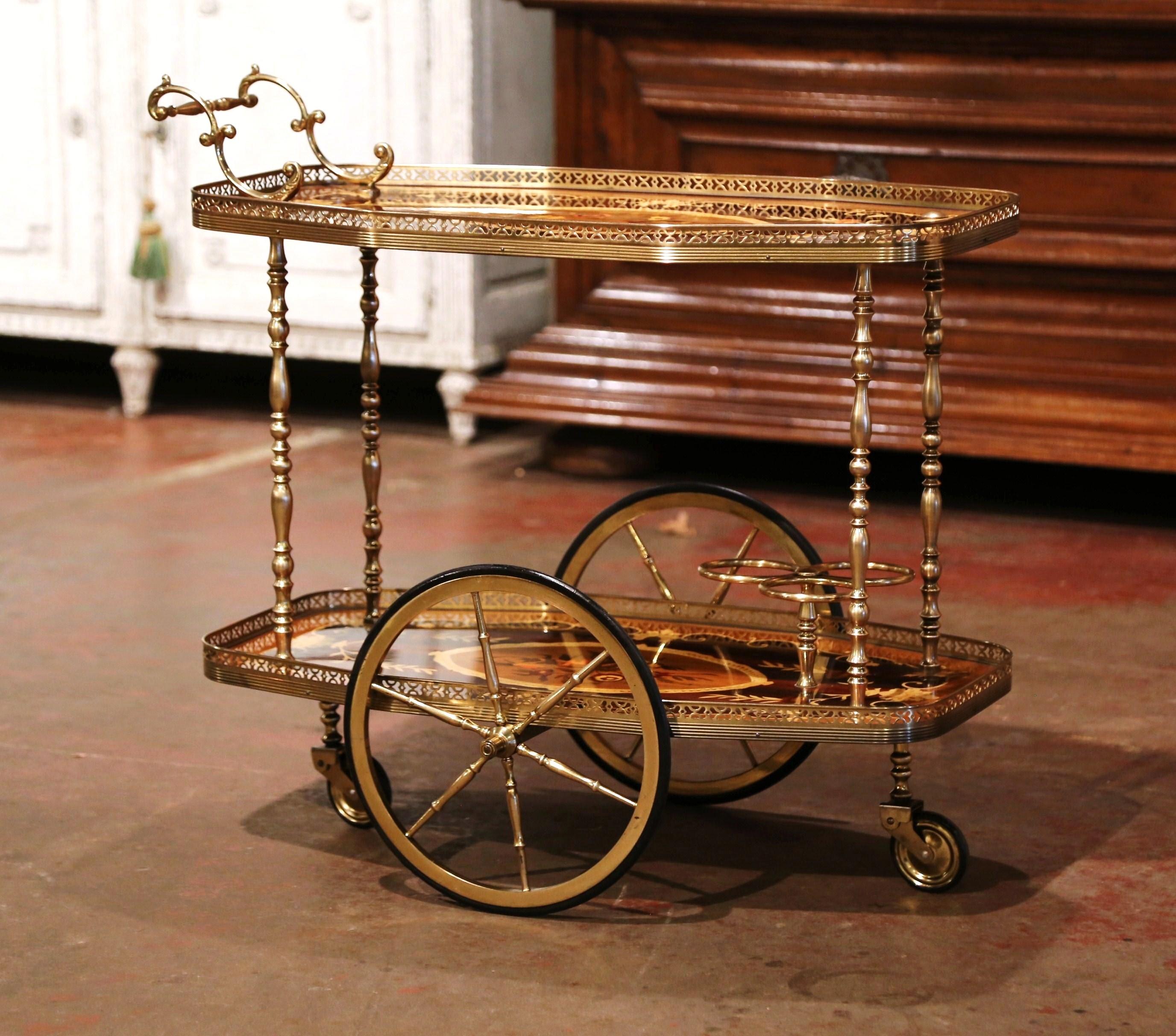This elegant two-tier wooden and brass cart was created in France, circa 1980. The cart sits on side spoke wheels and dressed with an elaborate brass handle at one end of the top deck. The two plateaus are decorated with marquetry inlaid medallions