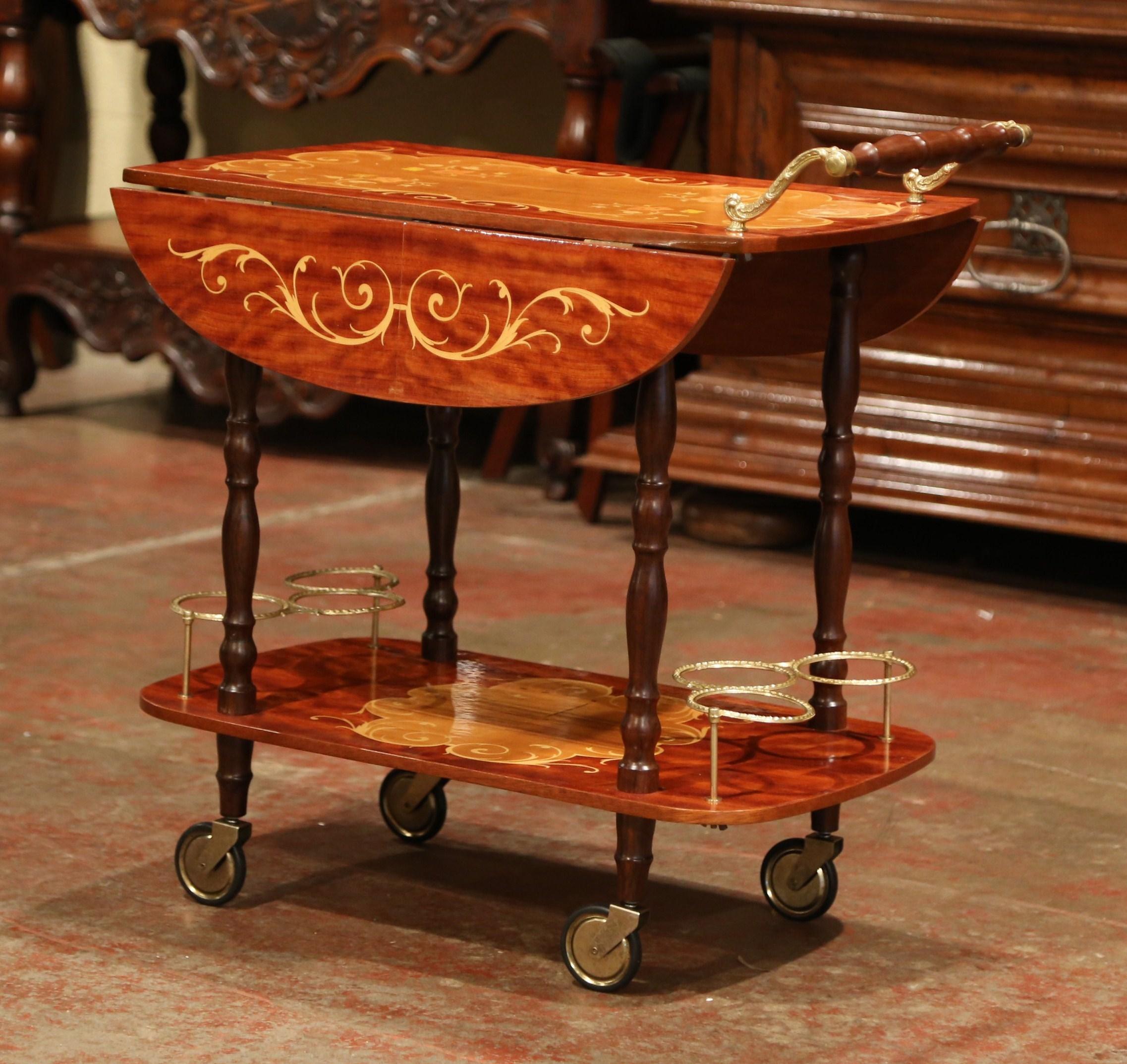 This fine wooden and brass cart was created in France, circa 1980. The brass cart sits on four wheels and features a large wooden and brass handle on one side. The two decks are connected with four turned spindles, and are decorated with wonderful