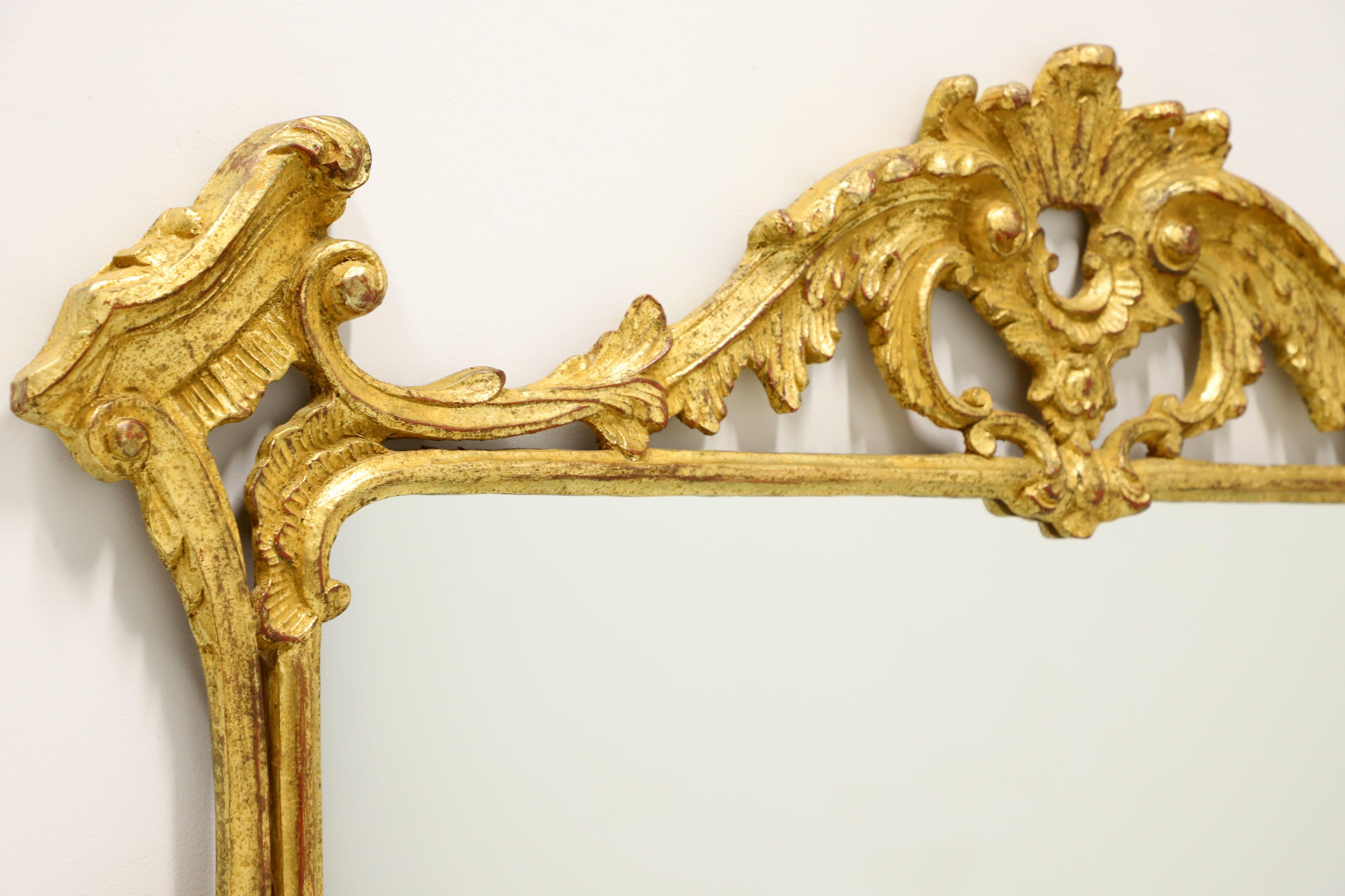 A French Rococo style wall mirror, unbranded. Mirror glass in an ornate gold gilt composite frame with exquisite design elements, acanthus leaves to top center & bottom sides, and other delicately carved ornamentation. Likely made in the USA, in the