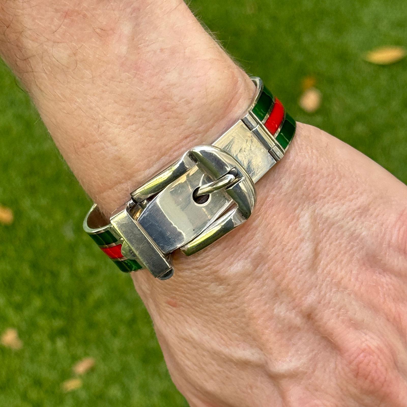 This late 20th-century Gucci enamel hinged bangle bracelet is a striking piece crafted in sterling silver and finished with vibrant red and green enamel detailing. Designed in the iconic buckle style, the bracelet features a 1-inch wide buckle
