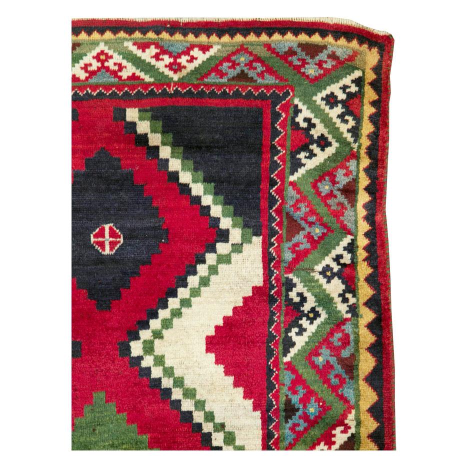 A vintage Persian tribal Gabbeh accent rug handmade during the late 20th century with a stepped diamond pattern in red with a green border. Other shades include dark blue that reads almost black, pale yellow, ivory, and brown.

Measures: 4' 6