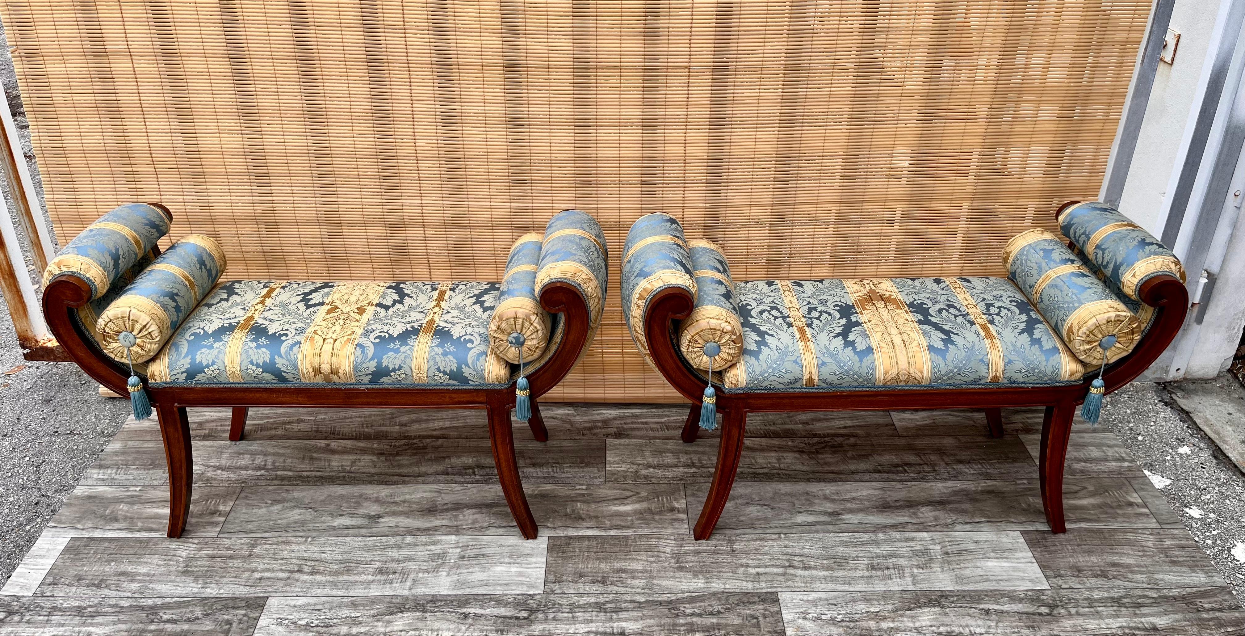 A Pair of Late 20th Century Hollywood Regency / Neoclassical Revival Style Window Benches. 
Feature a solid wood carved frame with scroll armrests and slightly curved legs, upholstered with exquisite gold and blue fabric, and embellished with two