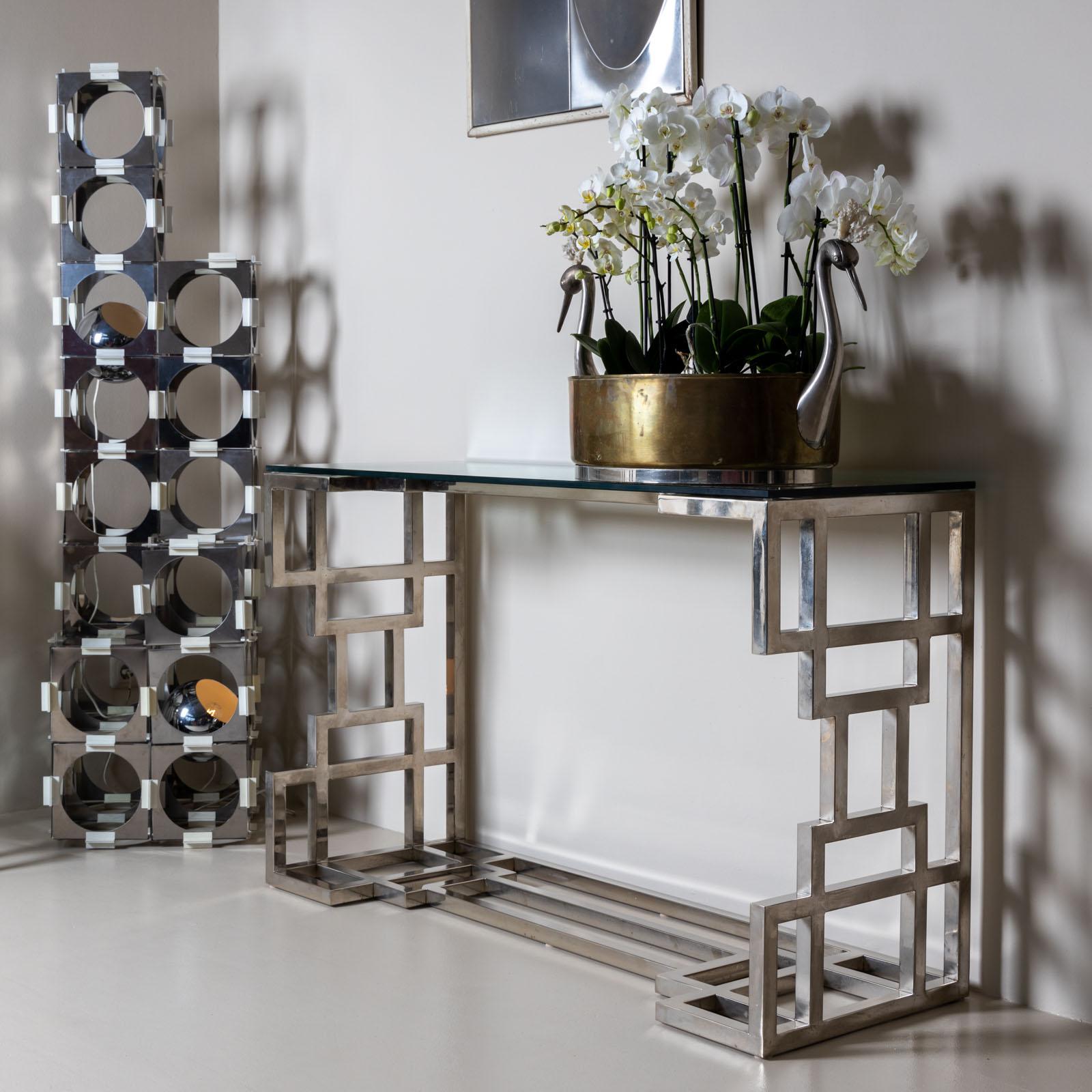 Ein Paar Wandkonsolen im Hollywood-Regency-Stil mit verchromten Metallrahmen und geometrischen Seitenwänden. Jede Konsole ist mit einer rechteckigen Glasplatte versehen. Ein charakteristisches Beispiel für die glamouröse Designästhetik der 1980er