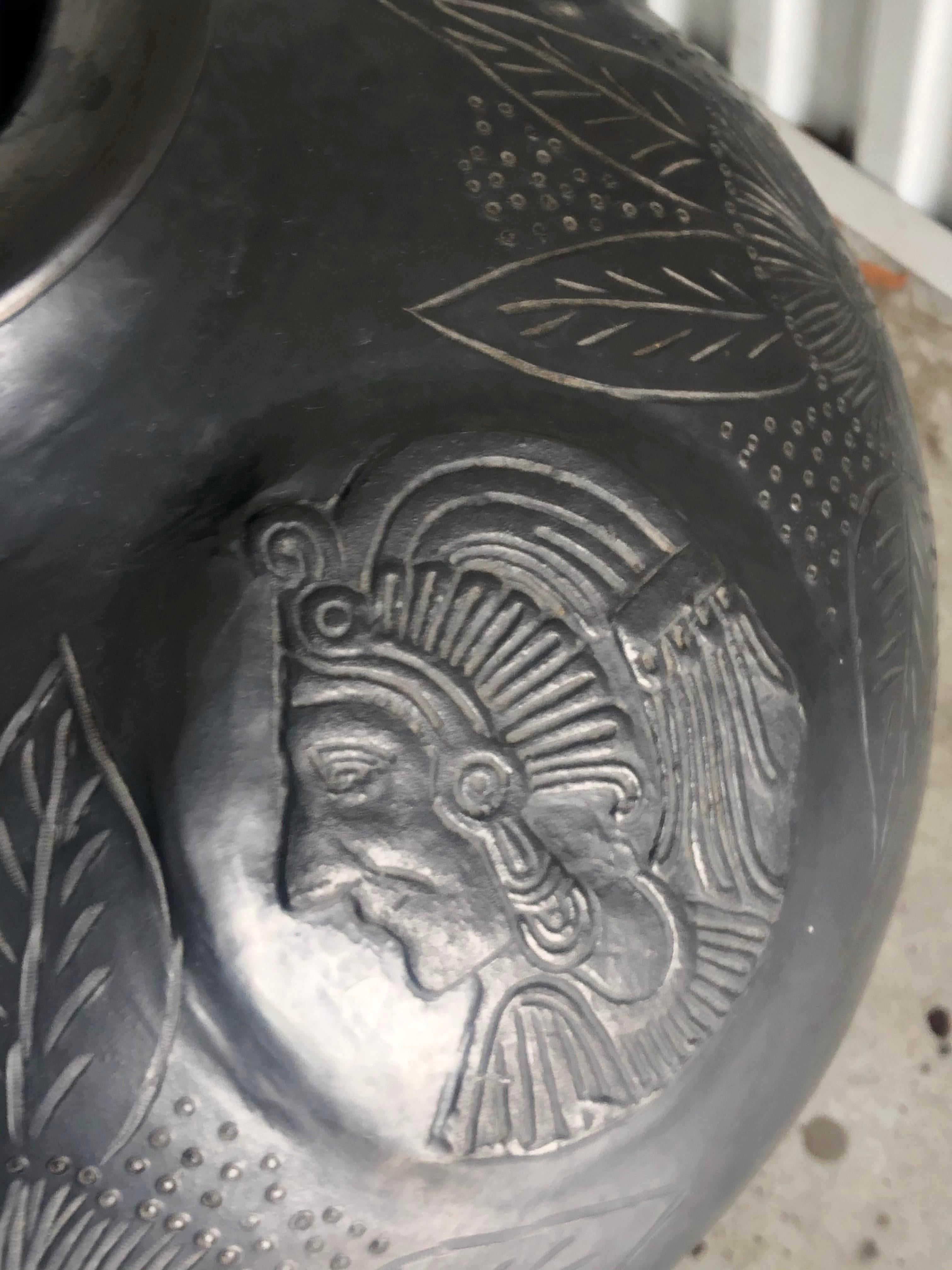 Amazing black pottery urn. In the manner of Pueblo pottery it has that famous sheen to the piece. Decorated with hand carved Indian heads and large flowers and leaves. Sits in a wrought iron ring. Acquired from a Wellington estate. 