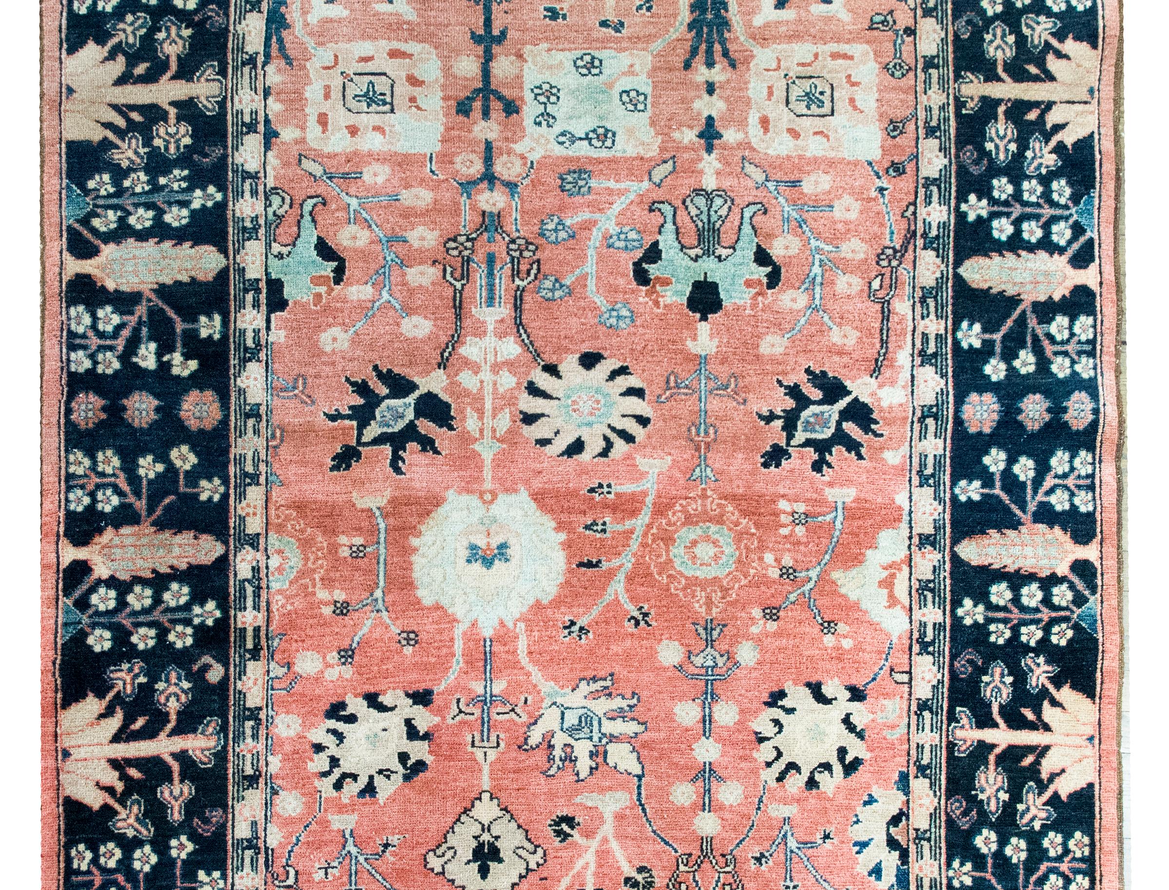 Questo tappeto vintage in lana indiana, annodato a mano alla fine del XX secolo, trae ispirazione dalla classica tradizione persiana Sarouk Farahan. Una disposizione asimmetrica di fiori di grandi dimensioni e di rampicanti si estende su un campo di