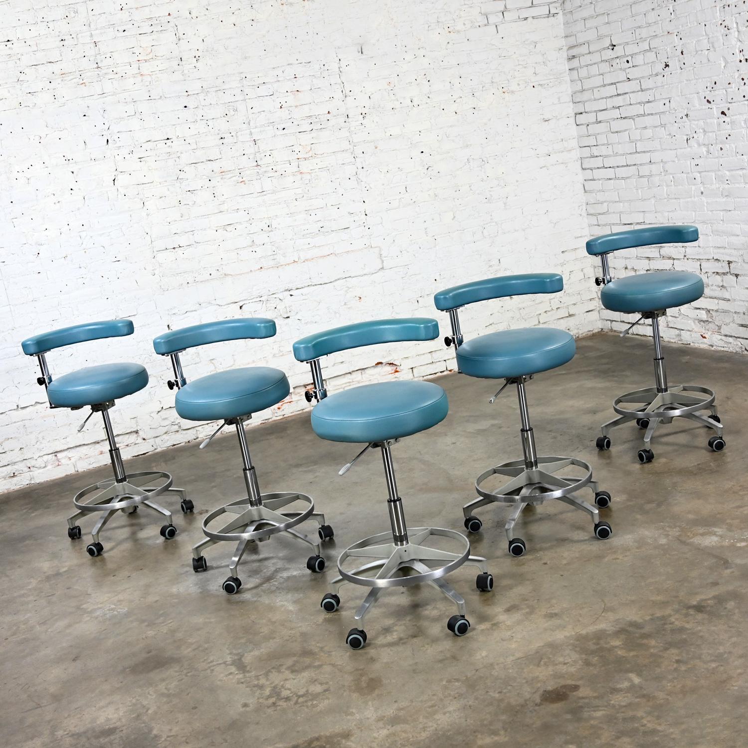 Awesome vintage Industrial medical or dental barstools by A-Dec with steel blue faux leather and adjustable height & swivel, set of 5. Comprised of chrome arm/seat & lower base shaft, cast aluminum ring footrest & 5 prong base on black & gray