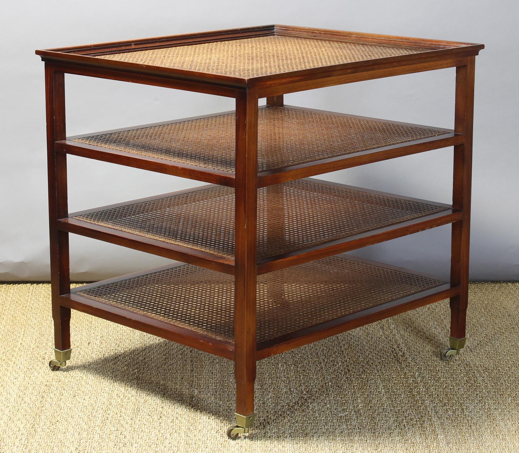 A classic late 20th century. 4-tier mahogany étagère side table with cane shelving inset with glass top. The square tapered legs terminate into brass casters.