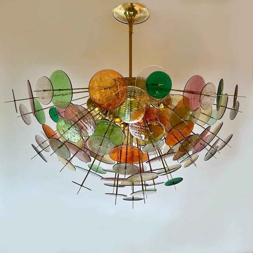 Important sputnik chandelier with multicolored (beige, orange, pink, grey, light green and emerald green) glass disks of two sizes: 20 & 13 Diam. cm. 
14 E14 Light Bulbs covered from brass caps.