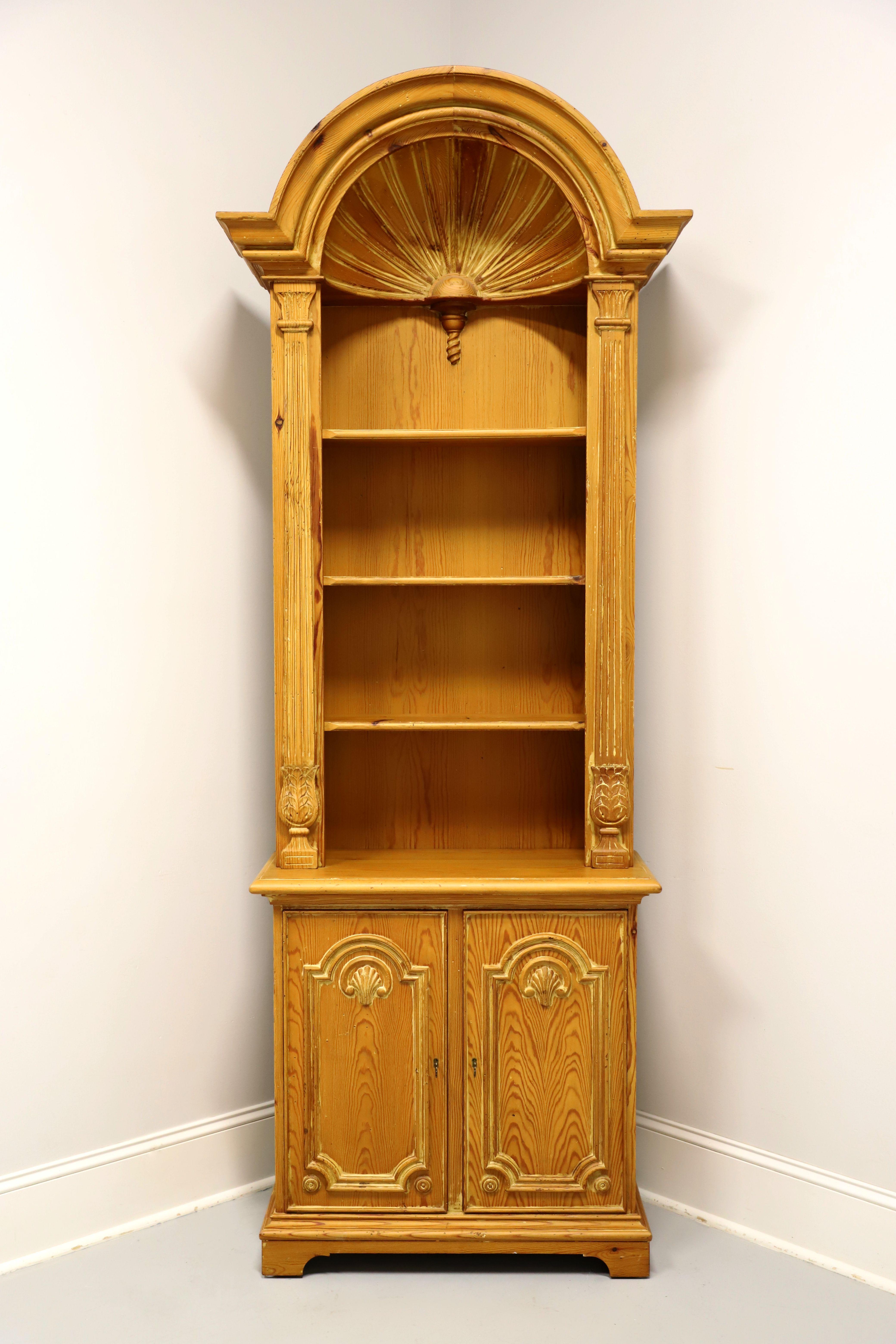 A Neoclassical style bookcase with cabinet, unbranded. Solid pine with slight distressing, brass lock hardware, intricately carved arched top, carved & fluted side columns, ogee edge to cabinet top, and bracket feet. Features upper open bookcase