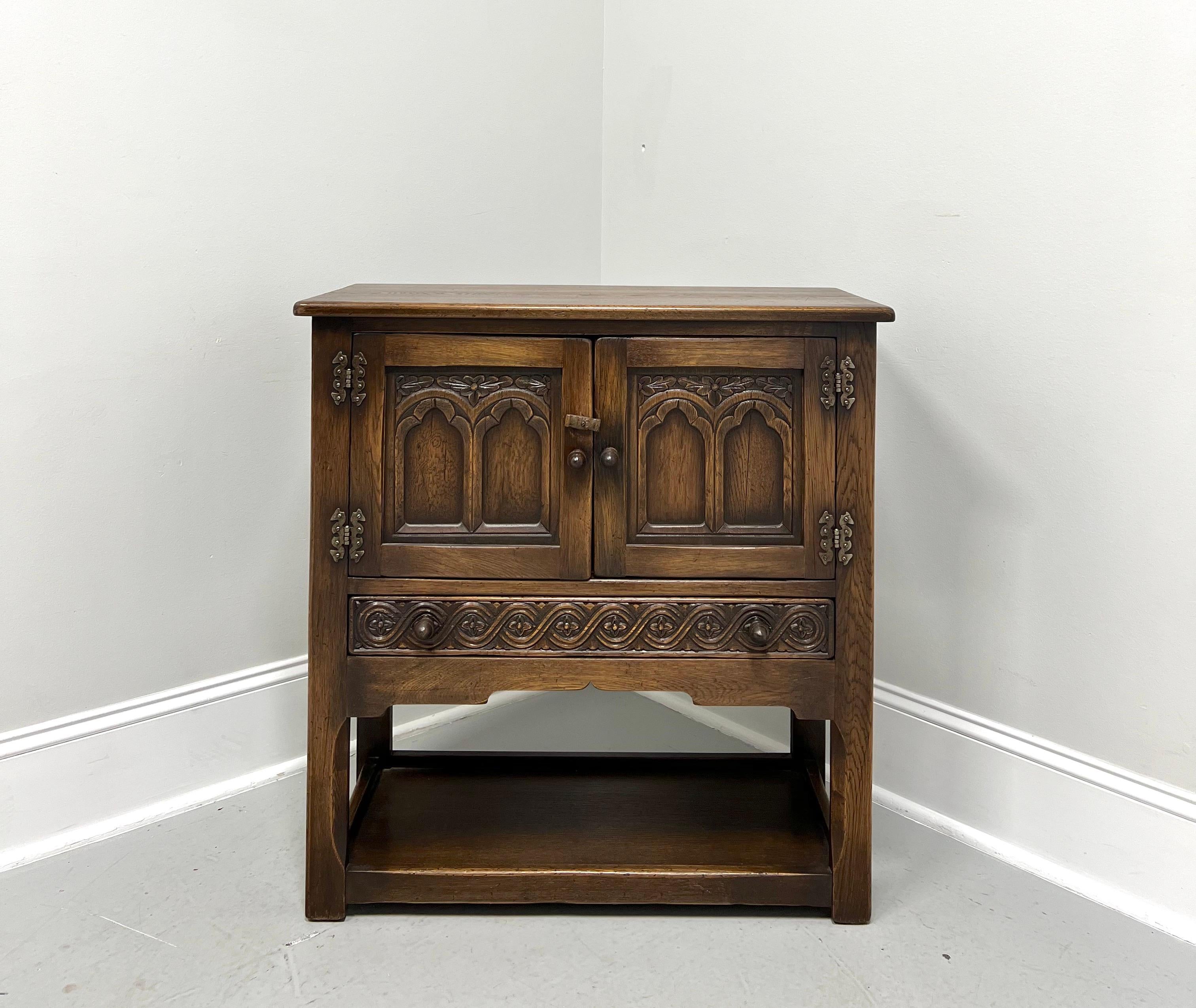 A Jacobean style console cabinet, unbranded. Solid oak with brass hinge hardware, bullnose edge to the top, decoratively carved door & drawer fronts with wood knobs, carved apron, open undertier floor level shelf, and carved straight legs. Features