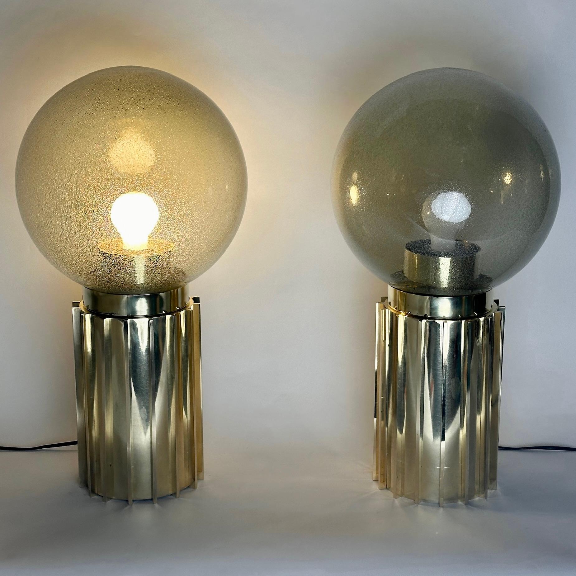 This pair of modern table lamps with smoked grey Pulegoso Murano art glass globes fit almost any kind of environment and they are perfect to be placed either on night stands or for any leaving room.
The brass basement resembling a Doric column with