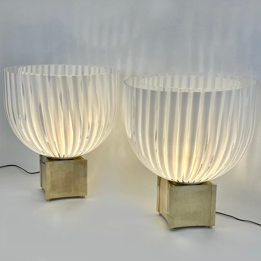 This pair of modern table lamps with transparent and striped white Murano art glass diffusers fit almost any kind of environment and they are perfect to be placed either on a statement entrance or for any leaving room.
The brass basement resembling