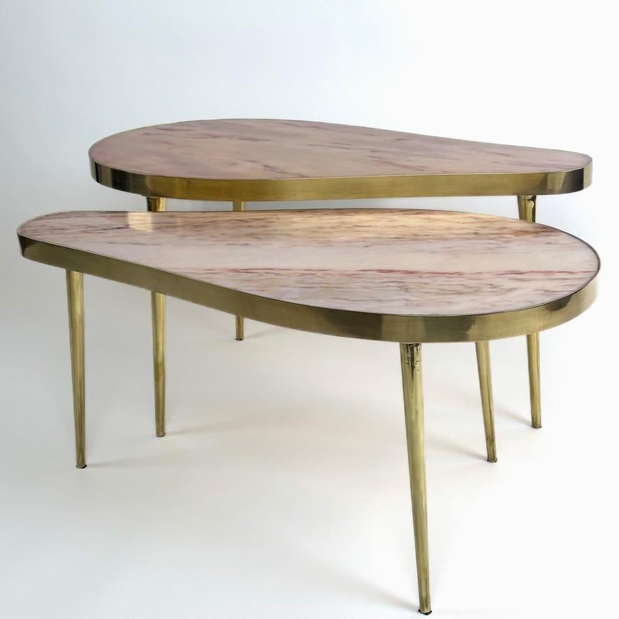 This curious pair of pear shape coffee tables can be displayed in several different manners in almost any modern or classic living room. The tables have three solid brass legs each and the onyx tops are framed with brass as well. They both can be