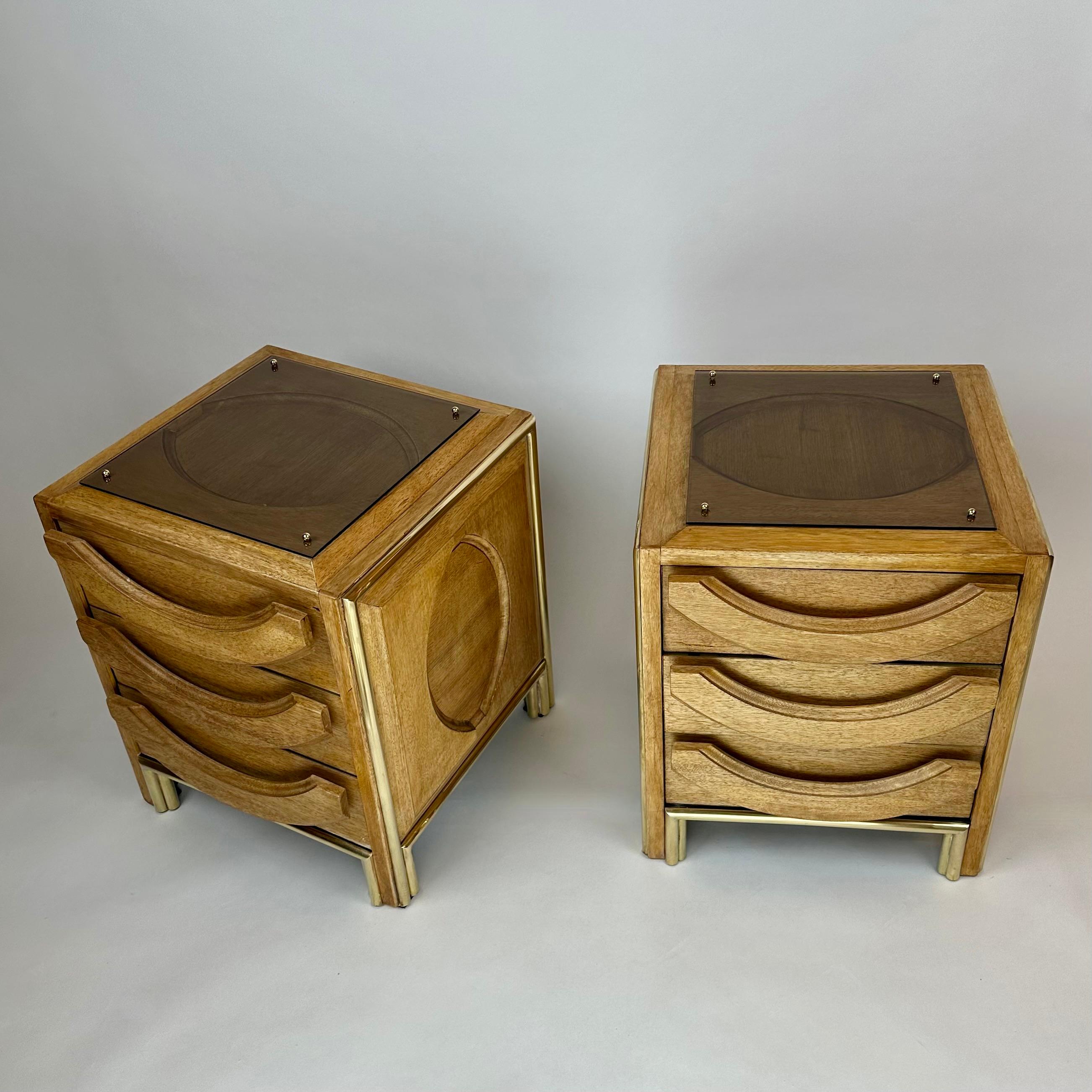 Captivating and stylish pair of beech wood, light brown removable glasses and brass details night stands. Eye motif in high relief on the top and on the laterals of the cabinets. Three drawers with solid wood handles, grey velvet paper and brass