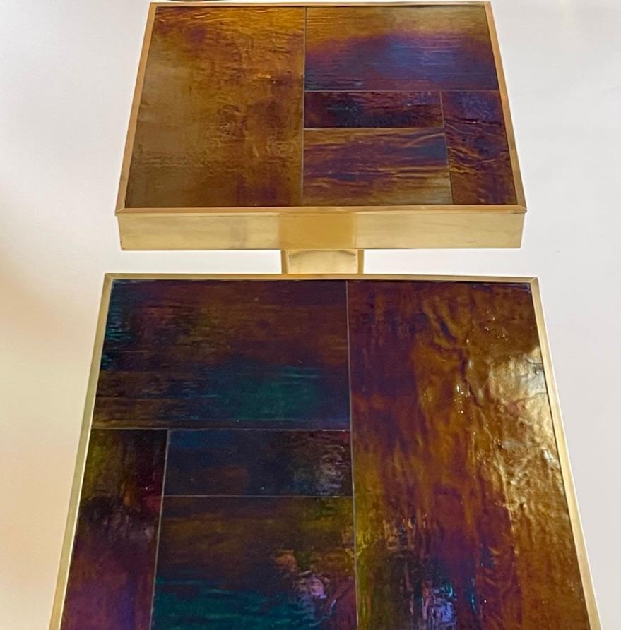 Pair of stunning side tables / night stands with an iridescent blue w/ gold shades Murano Art Glass Tops circled by brass bands.
While the left & right brass basements of the tables have several cubic shapes that intersect each other and giving to