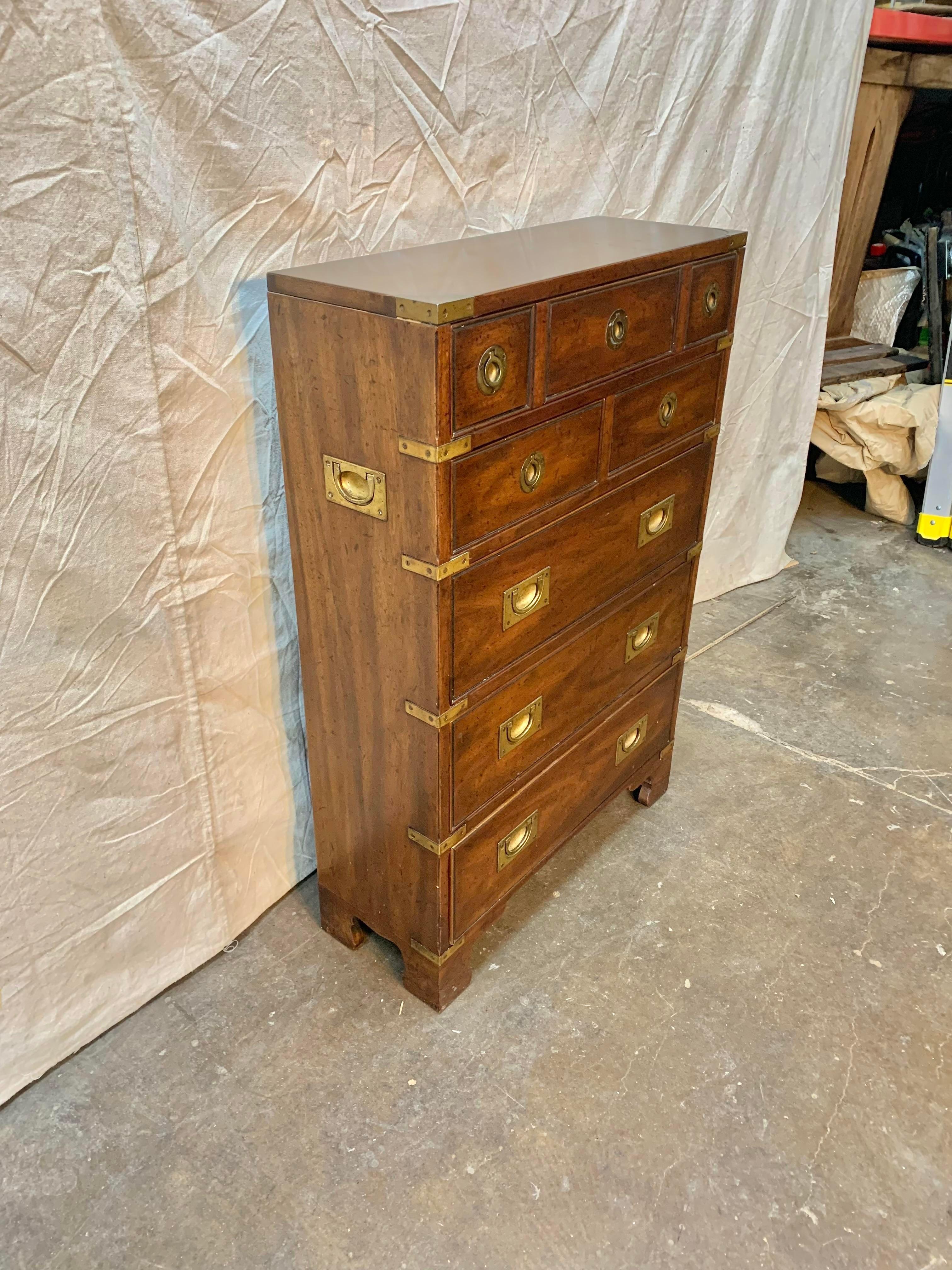 This Petite Campaign Chest was manufactored by Heritage in the late 20th century. The chest of drawers is crafted of walnut in warm hues and is brass bound and accented with inset brass hardware. The piece features 6 drawers, one large drawer at the