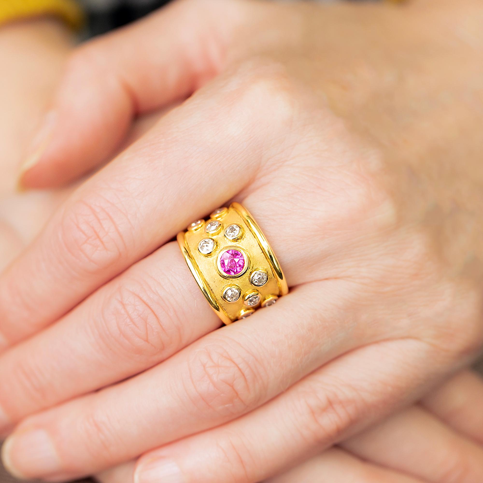 A late 20th century dress ring featuring a bezel set central pink sapphire with Victorian old cut diamonds to each side upon a matt textured finish which follows through on the whole ring. Edging the centrepiece is raised polished rounded edges to