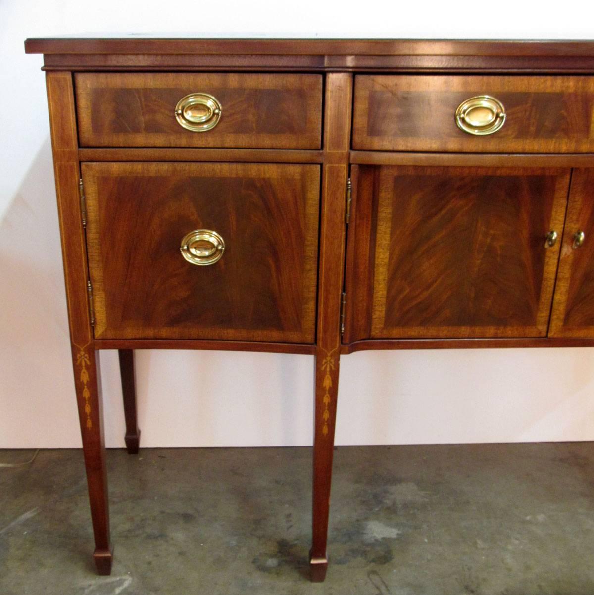 Late 20th century sideboard in the typical South Carolina style, mahogany with rosewood banding, bell flowers on the tapered legs above spade feet, and brass hardware. The silver cloth in the centre drawer is labelled 
