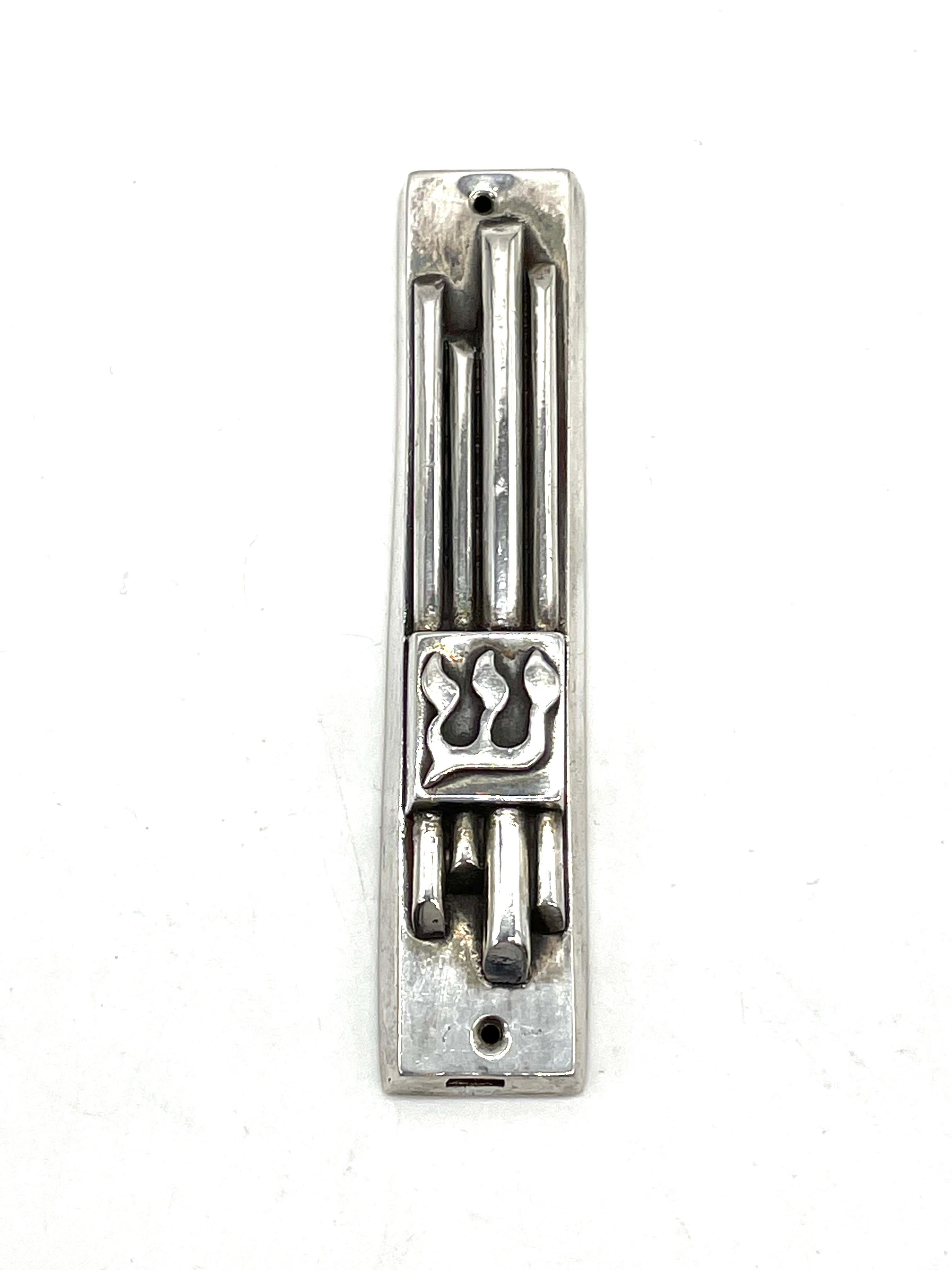 Pure silver mezuzah case by Henryk Winograd. Decorated with four vertical tubes, the Hebrew letter Shin referring to g-d appears at its bottom.

Henryk Winograd was one of the world's greatest 20th Century masters of traditional silversmithing