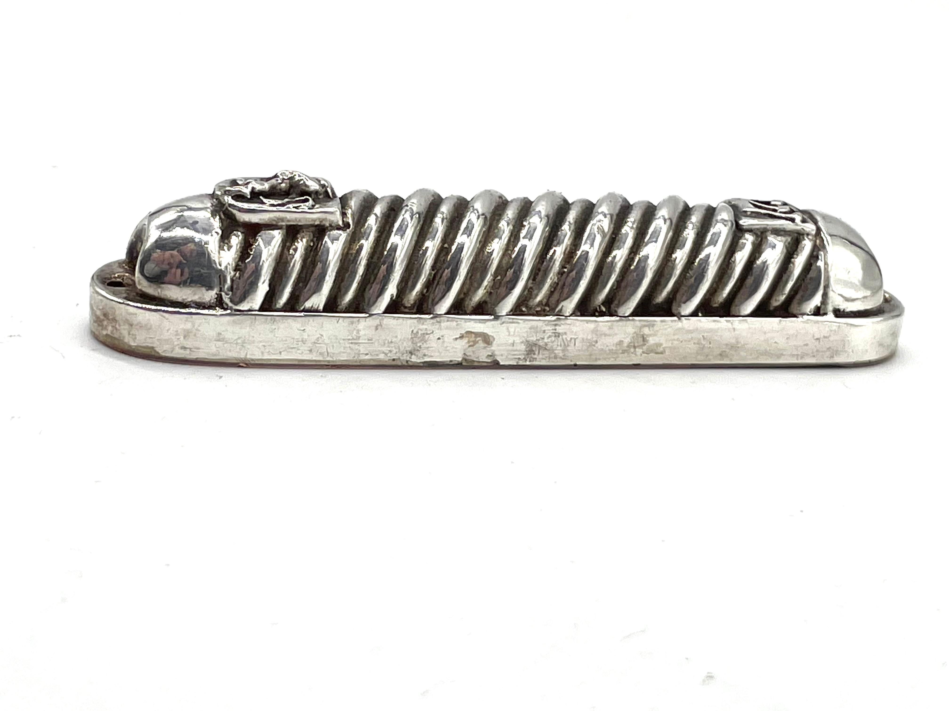 Pure silver mezuzah case by Henryk Winograd. Decorated with spiral motives, the Hebrew letter Shin referring to g-d appears at its top, while a lion referring to the Lion of Judea appears in its bottom. 

Henryk Winograd was one of the world's