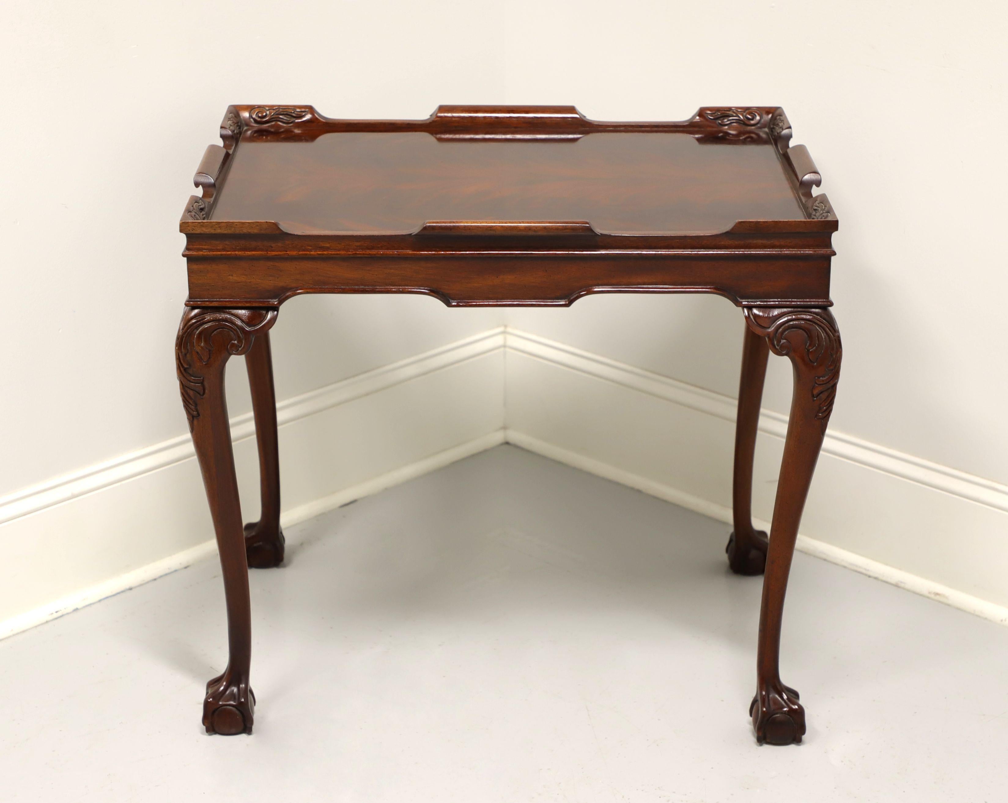 A tea table in the Chippendale style, unbranded, similar quality to Baker or Henredon. Mahogany with flame mahogany top surface, a gallery, carved apron, cabriole legs, carved knees and ball in claw feet. Features two slide out trays with brass