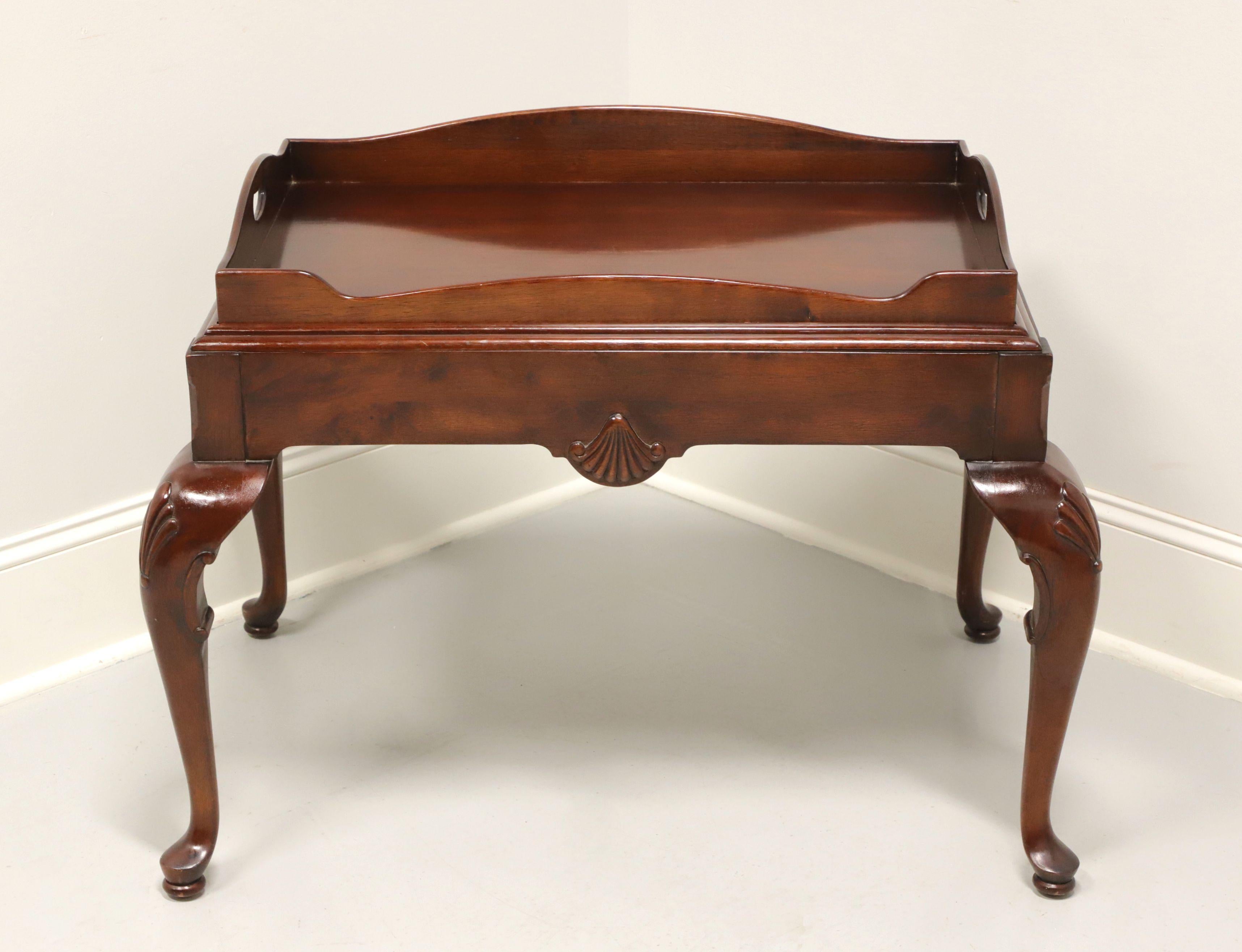A tea table in the Georgian style, unbranded, similar quality to Baker or Henredon. Solid mahogany with butlers tray top with open handles, apron with carved shells, shell carved knees, cabriole legs, and pad feet. Features removable butlers tray