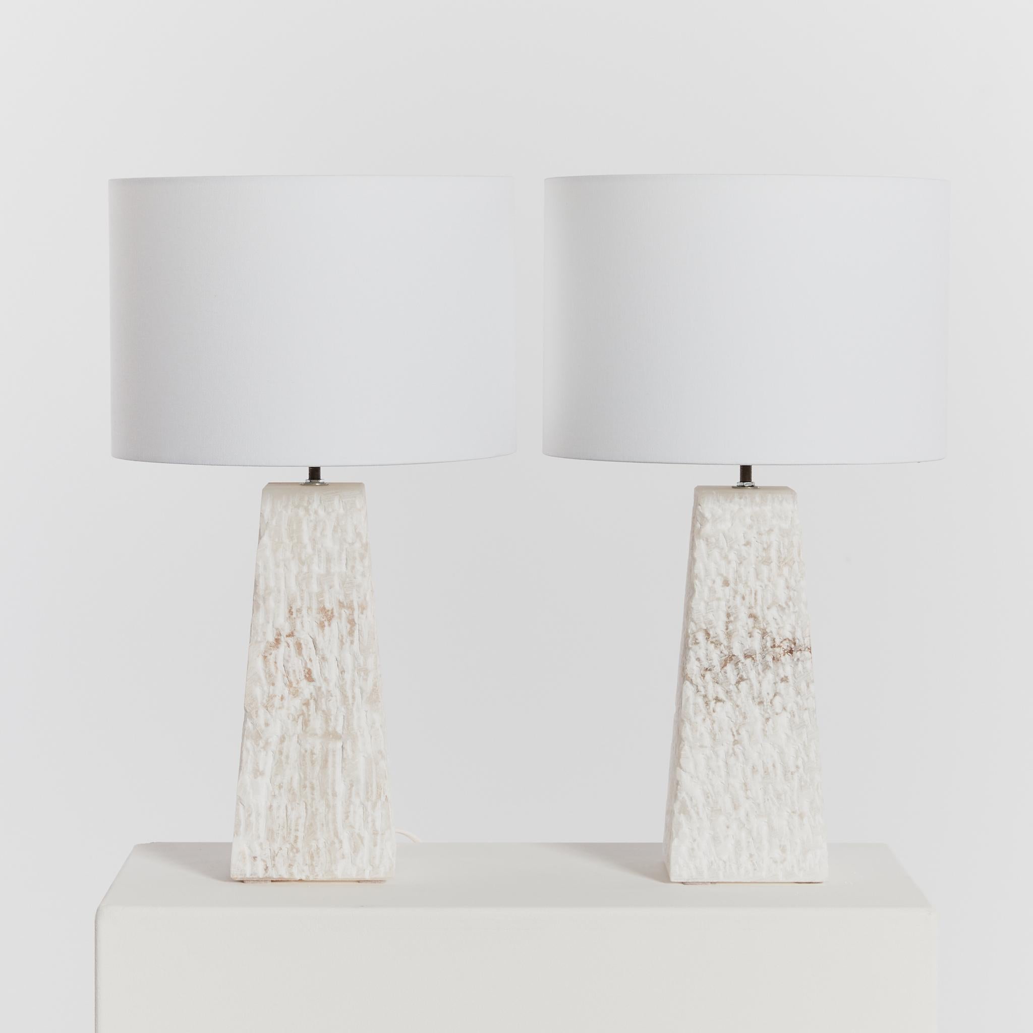 Pair of sculptural stippled stone lamps with trapeze form. Each carved from a single piece of Spanish alabaster, these statement lamps each include a new linen lamp shade.

This pair came from a town in Spain known for its alabaster quarry, which is