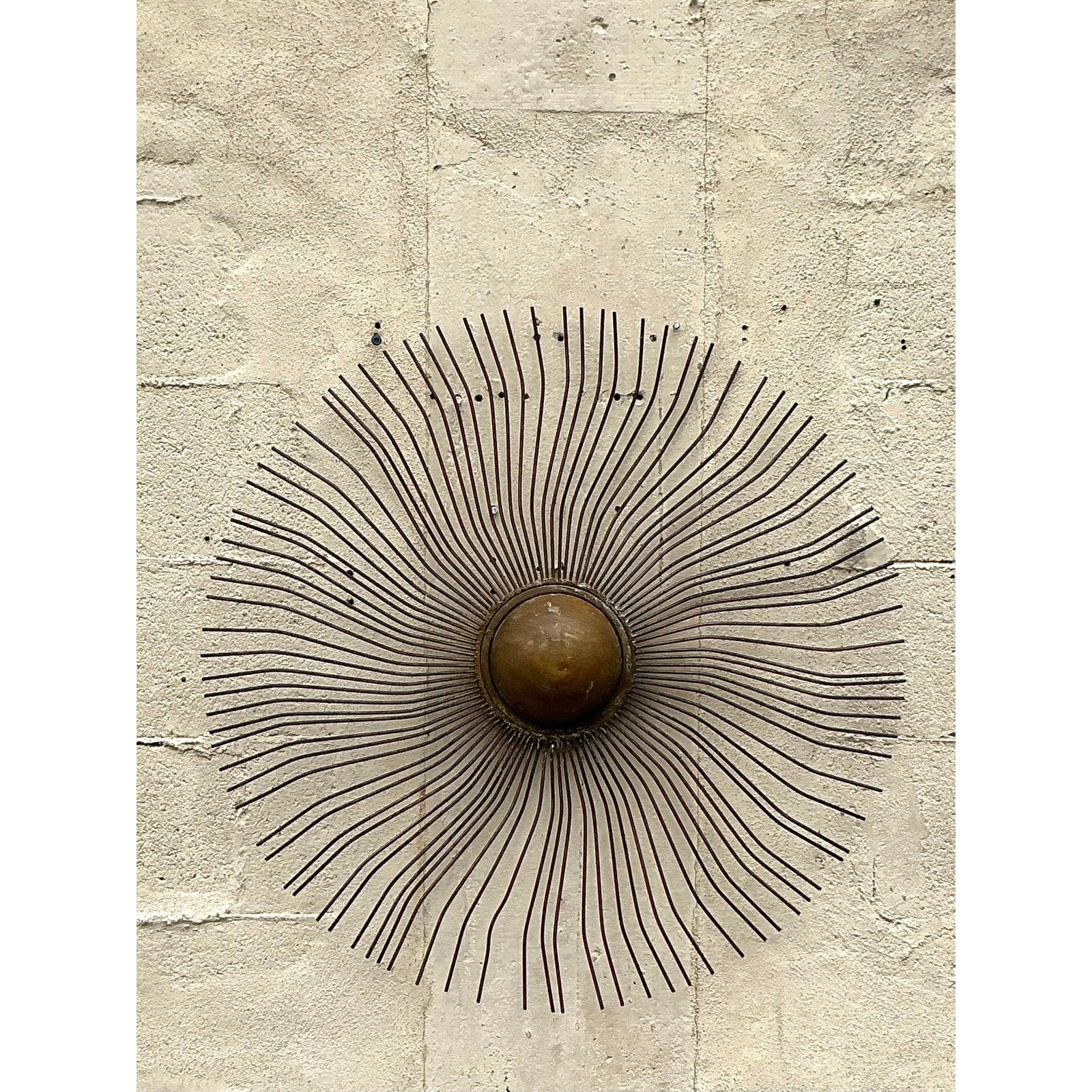 Infuse warmth and artistic charm into your space with this striking vintage boho-style sunburst wall sculpture. Crafted from delicately curved metal rods radiating from a central domed core, this piece embodies mid-century modern and bohemian