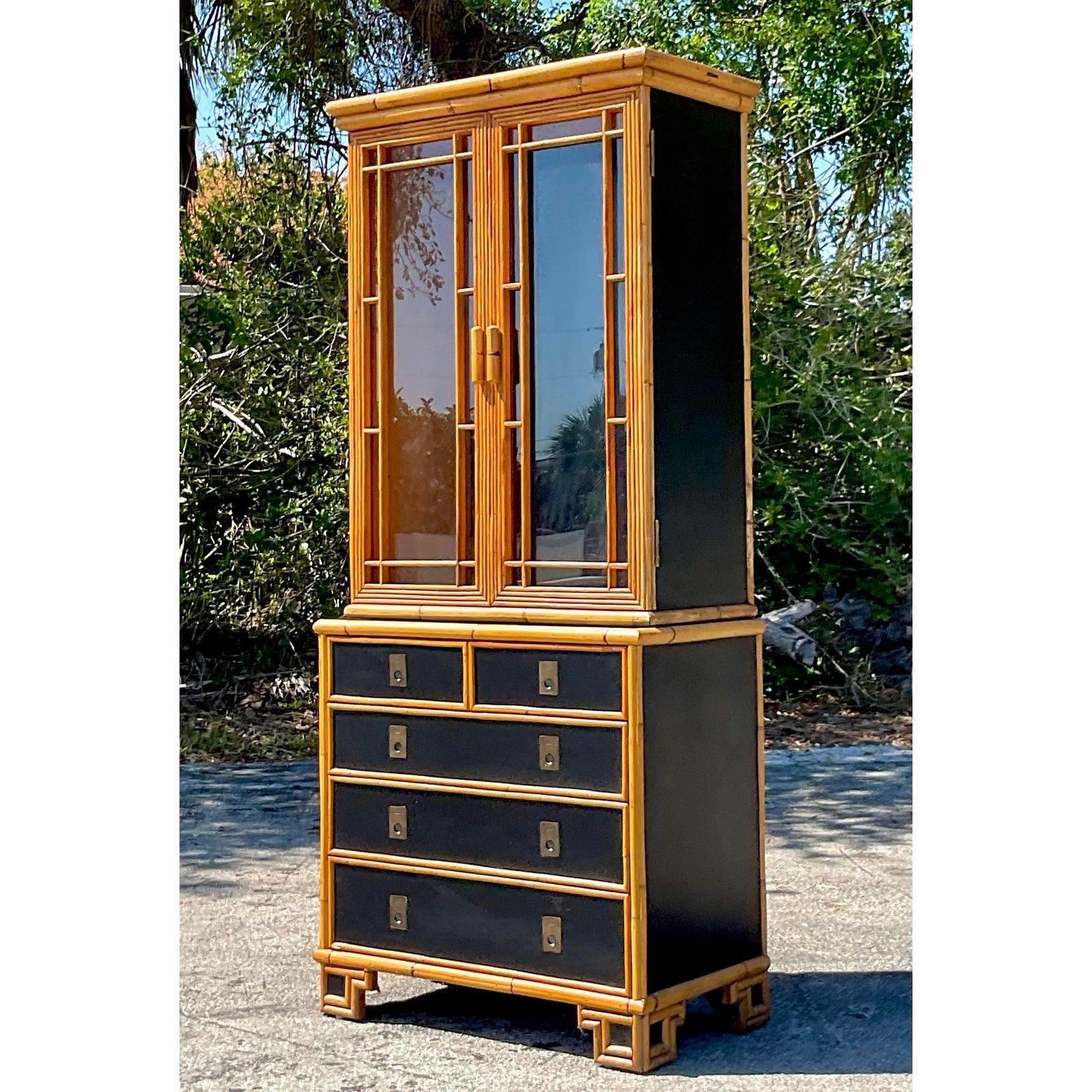 A stunning vintage Boho display cabinet. Chic rattan trimmed frame with lacquered insert panels and brass campaign hardware. Acquired from a Palm Beach estate.