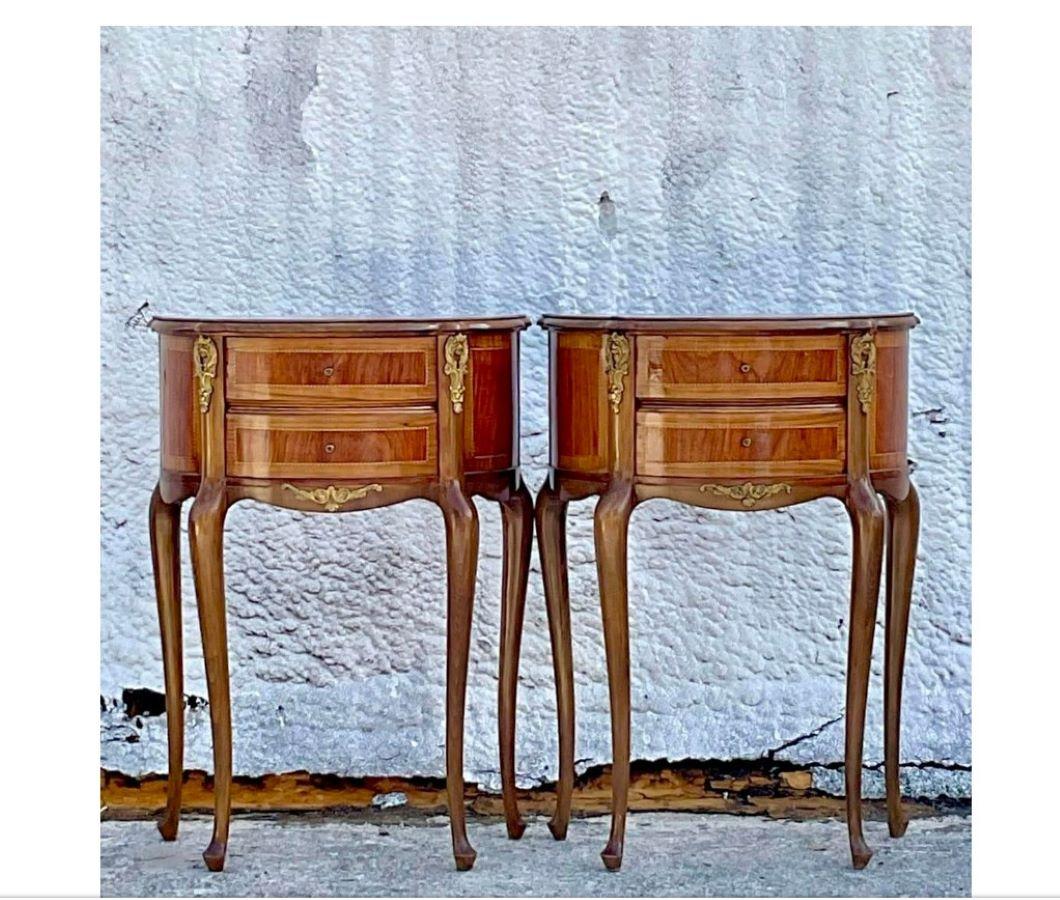 A stunning pair of wooden vintage nightstands with brass detailing and ebony inlay. They are taller than your usual nightstands and have two small drawers to keep all your personal items. Acquired at a Palm Beach estate. 