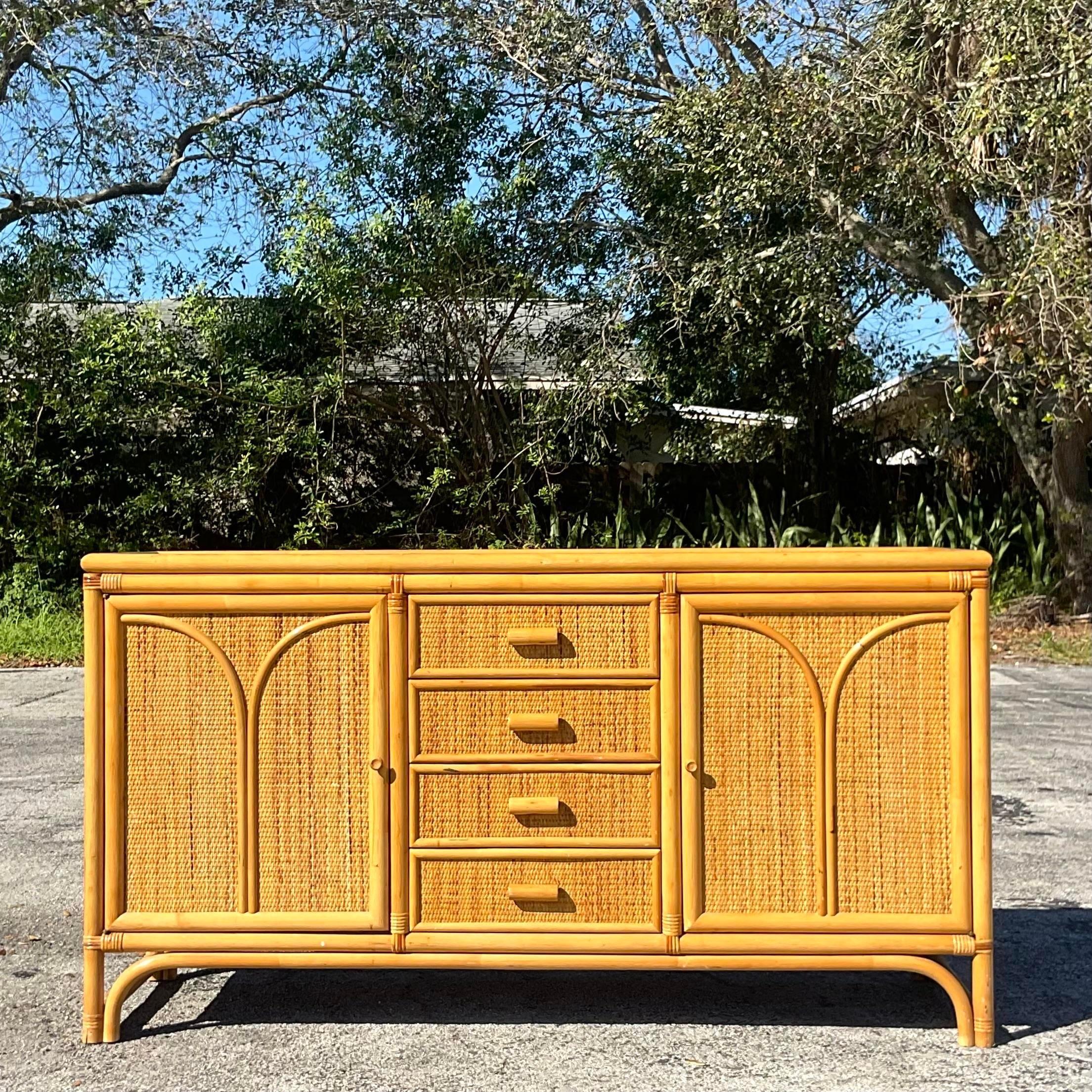 Vintage Coastal woven rattan credenza. A chic two door design with arched rattan and woven rattan inset panels. Lots of great storage below. Acquired from a Palm Beach estate.