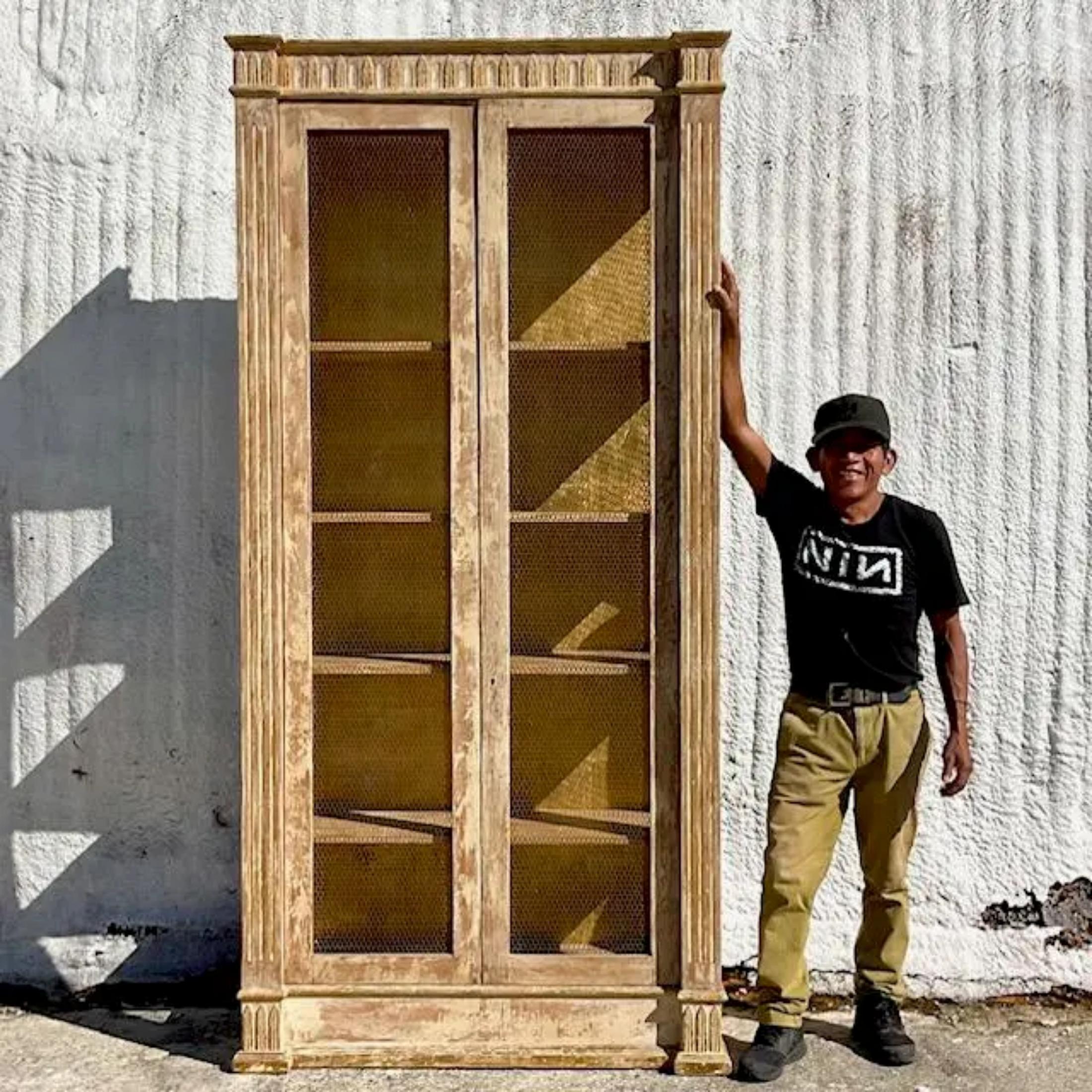 A spectacular vintage Boho Monumental etagere. A chic distressed cabinet with hand placed gold leaf interior. Inset wire door and side panels. Tall and impressive. Acquired from a Palm Beach estate
