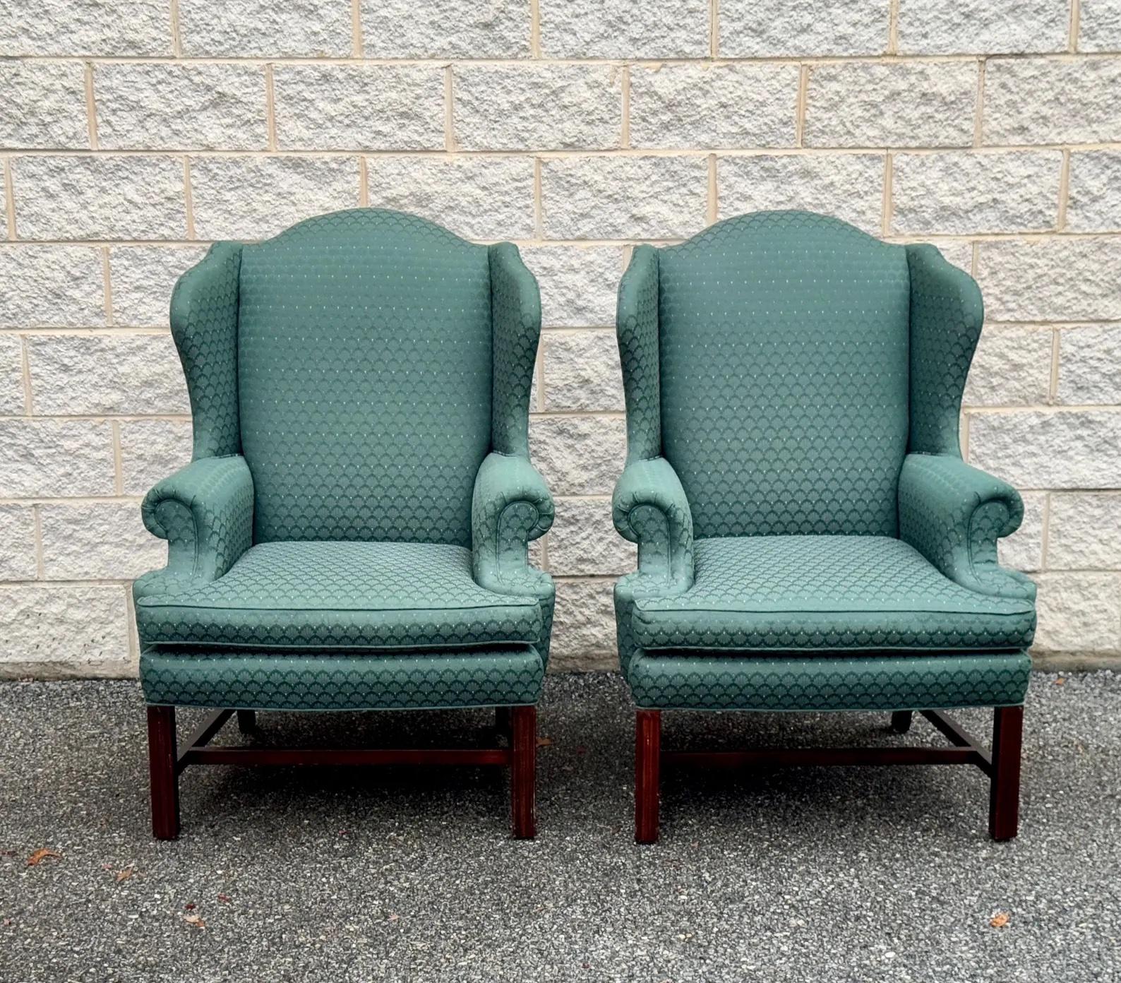 A beautiful pair of vintage wingback chairs featuring elegant green jacquard upholstery with an intricate scallop pattern. These classic high-back chairs have rolled arms, sturdy wooden frames, and cabriole-style legs. They offer both comfort and