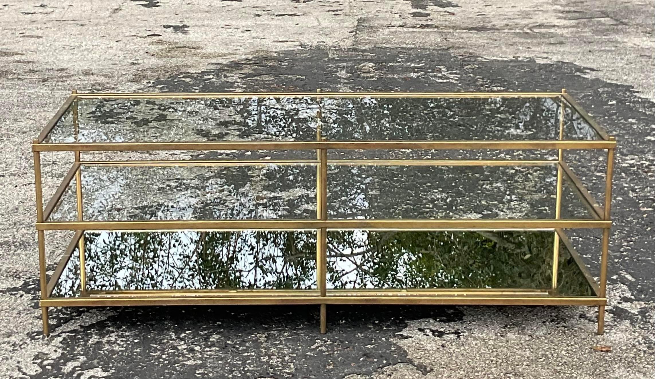 A fabulous vintage Regency coffee table. A chic burnished brass with inset glass shelves. Thr lowest level is a mirrored shelf. A chic and simple design. Acquired from a Palm Beach estate.