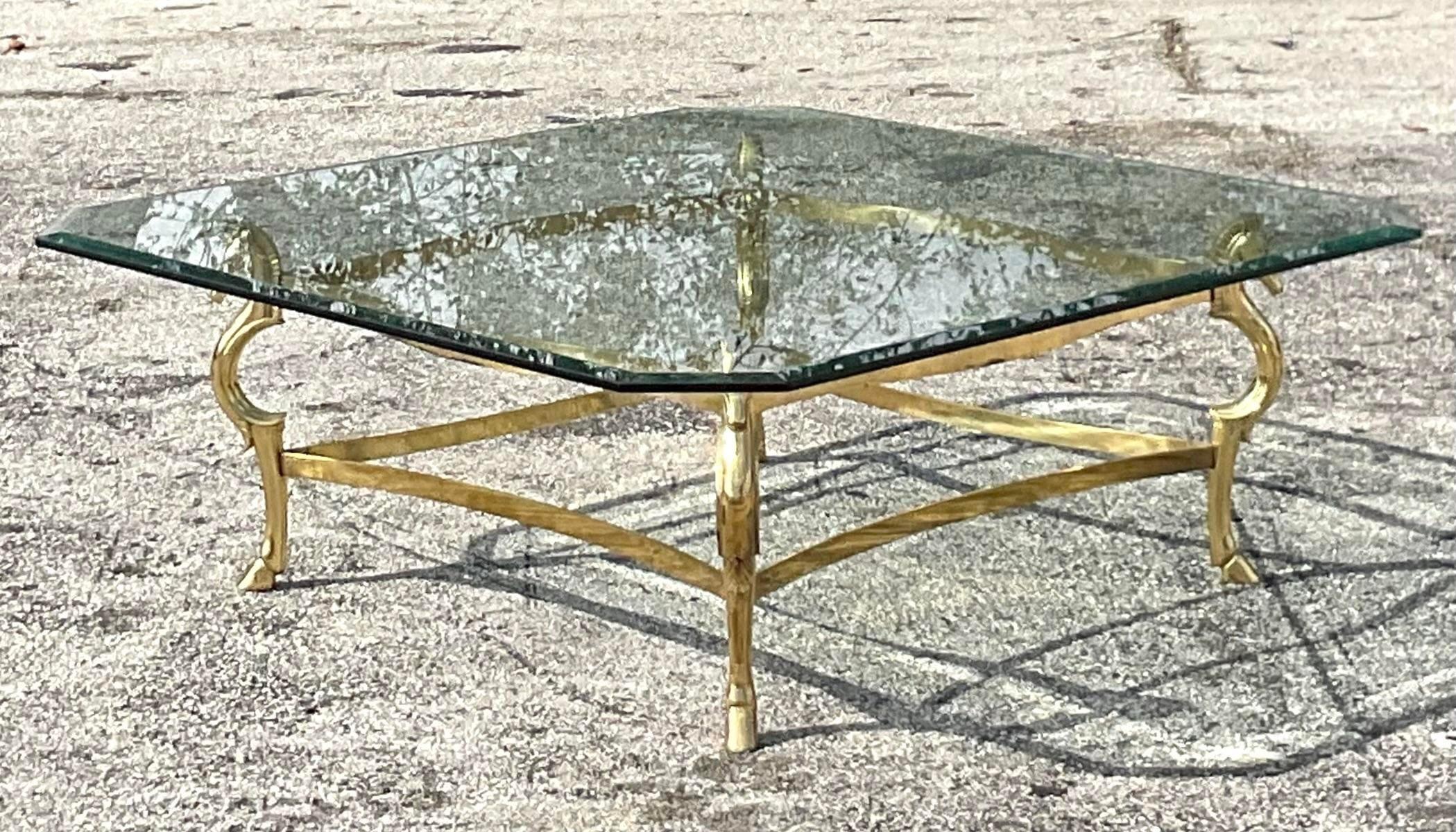 A stunning vintage Regency coffee table. A chic polished brass frame in a beautiful horse head design. Notch corner beveled glass top. Done in the manner of Maison Jensen. Acquired from a Palm Beach estate. 