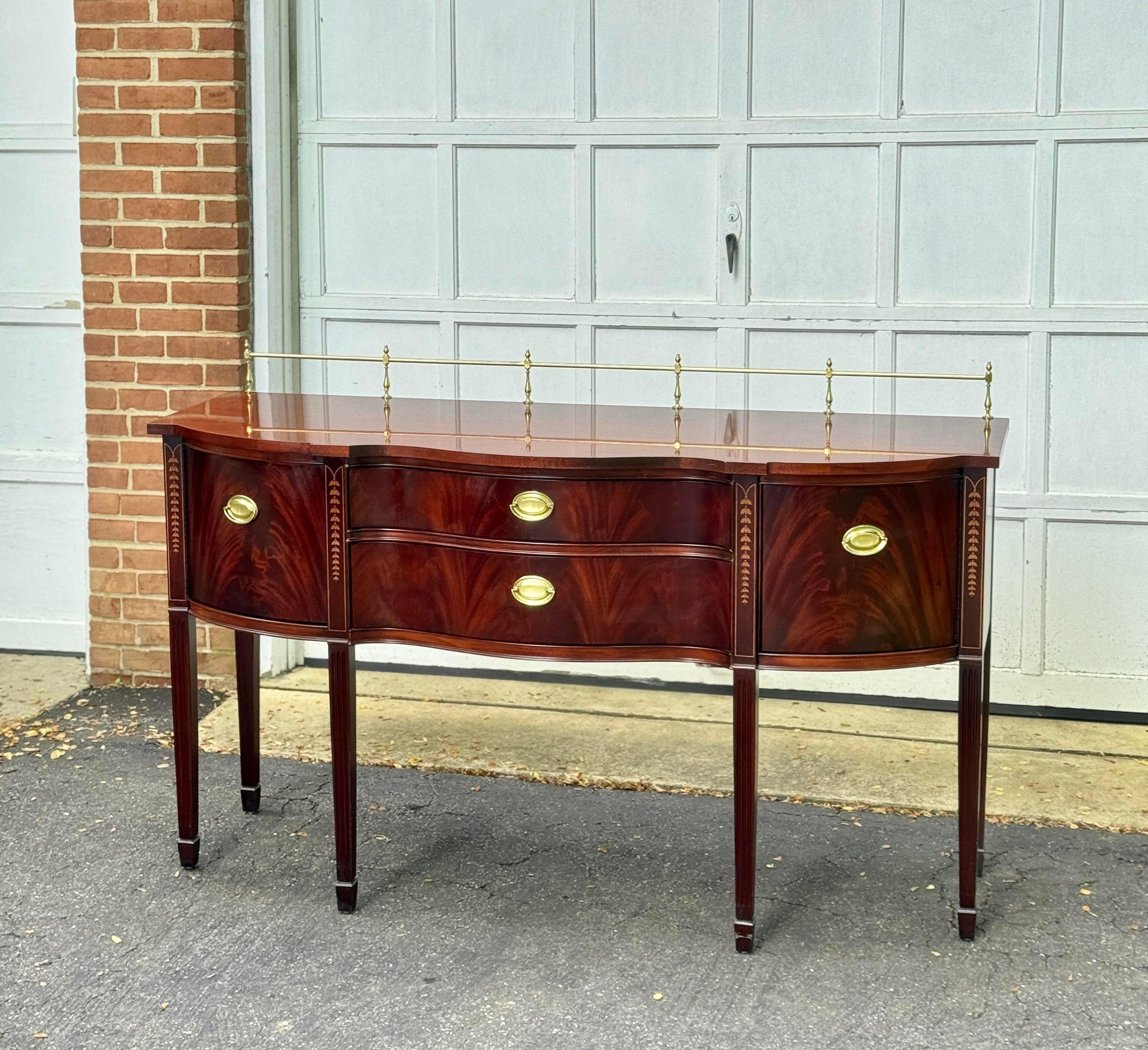 Features high-quality construction, beautiful flame mahogany and decorative inlays, cabinet doors on each side, two dovetailed drawers, Georgian brass hardware & gallery bar, and tapered legs with spade feet.