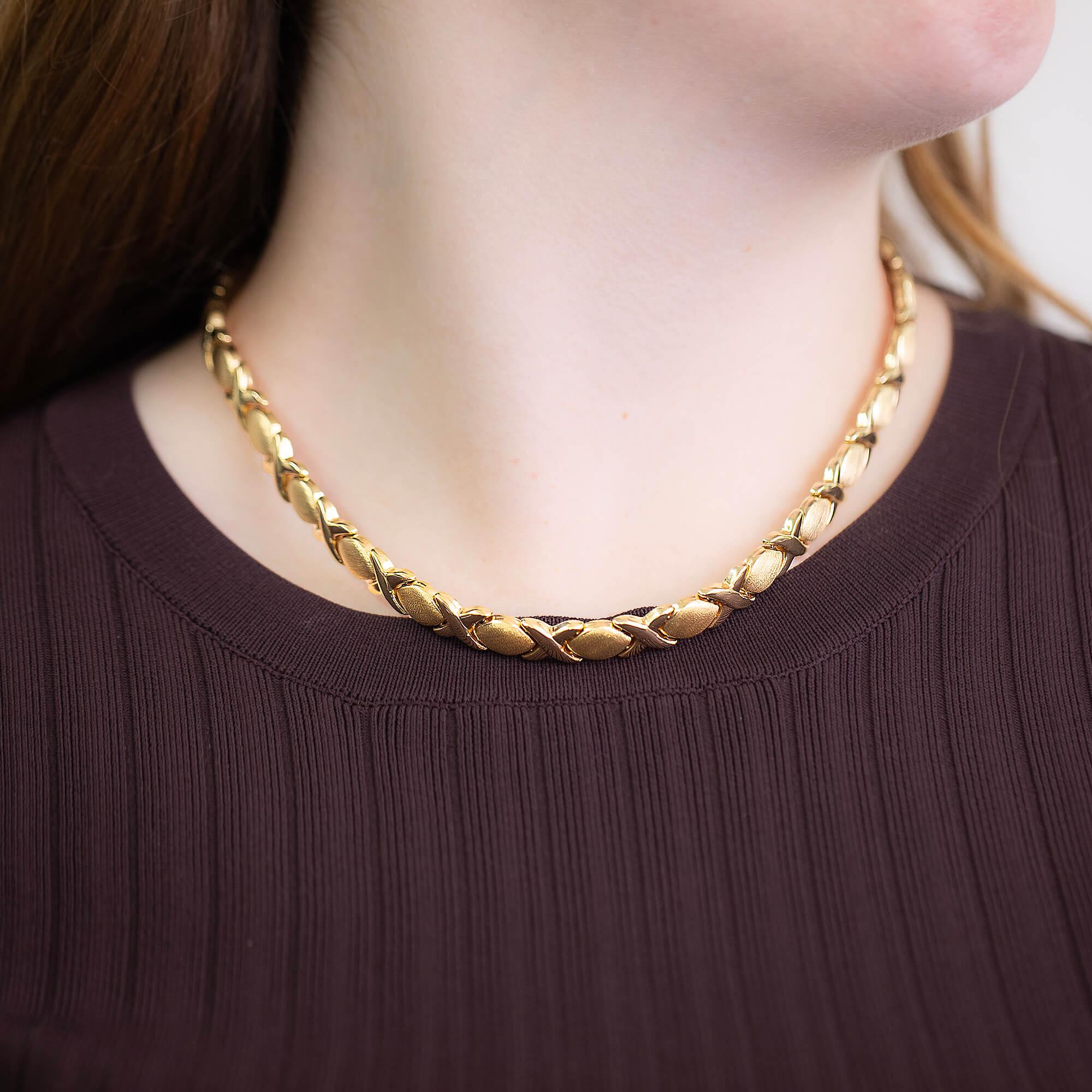Questo splendido collarino in oro giallo presenta una serie di baci incrociati lucidi con maglie a forma di marquise spazzolate tra ogni bacio. Le due texture conferiscono calore a questa collana d'oro. Chiuso da una fibbia a scatola e da un