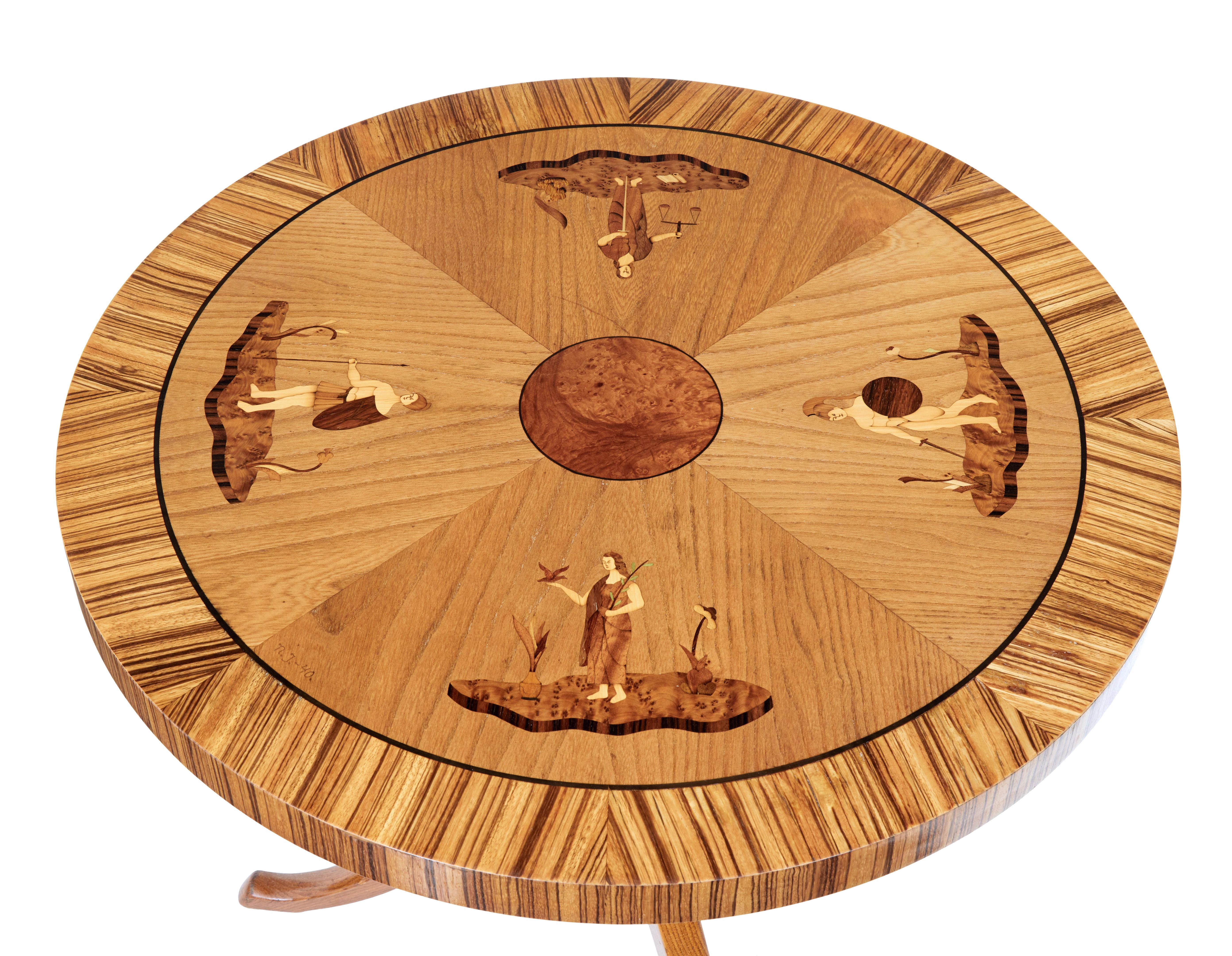 Late Art Deco Scandinavian coffee table, circa 1940.

Circular top, round burr centre surrounded by 4 mythical women on each quarter. Inlaid with walnut, rosewood and pear wood. Signed n.J with the date of '40.

Standing on an elm stem, 3 legs