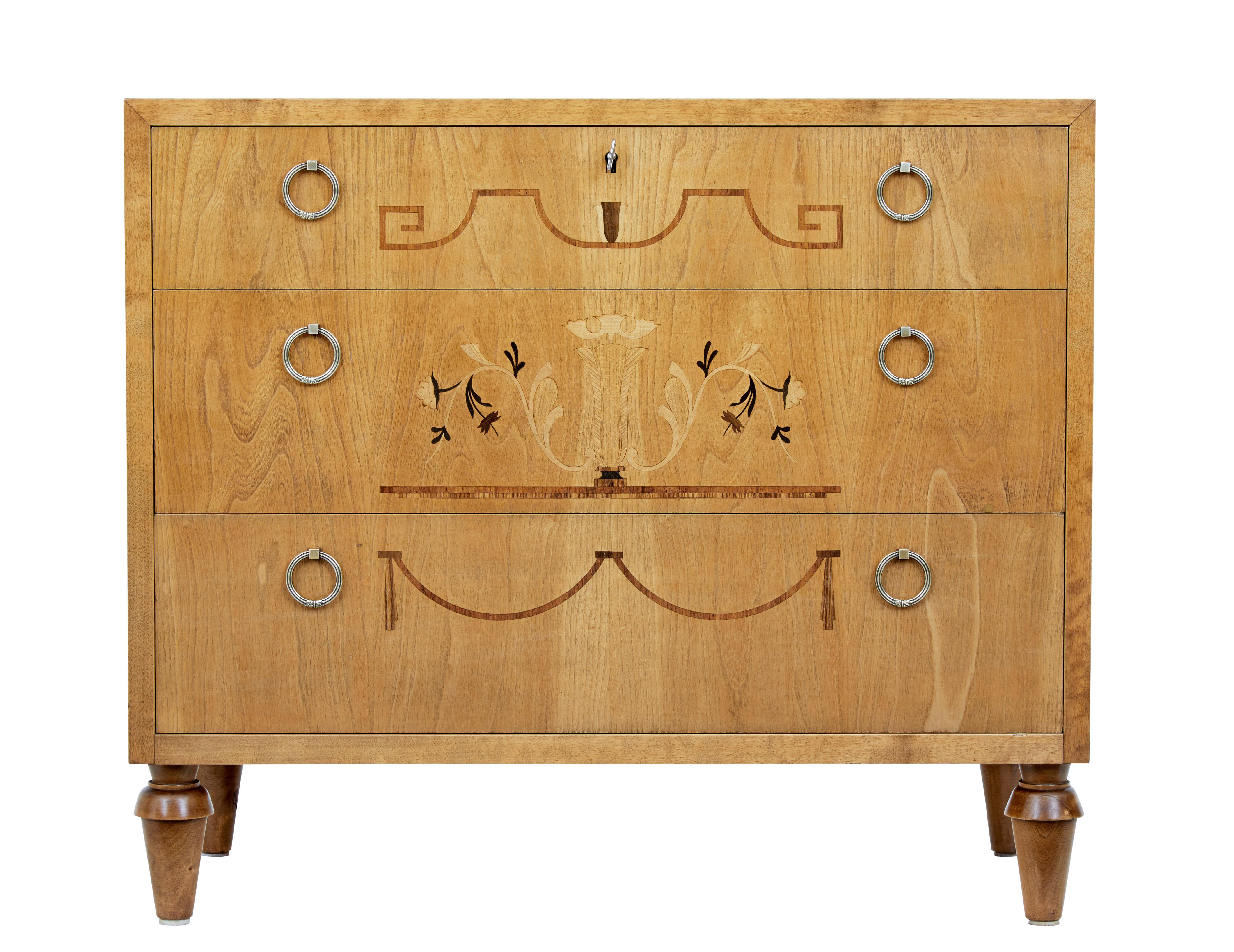 Late Art Deco inlaid elm and birch chest of drawers circa 1940.

Beautiful chest of drawers fitted with 3 graduating drawers. Each inlaid with classical designs in walnut and birch. Fitted with ornate ring handles.

Top drawer locking with