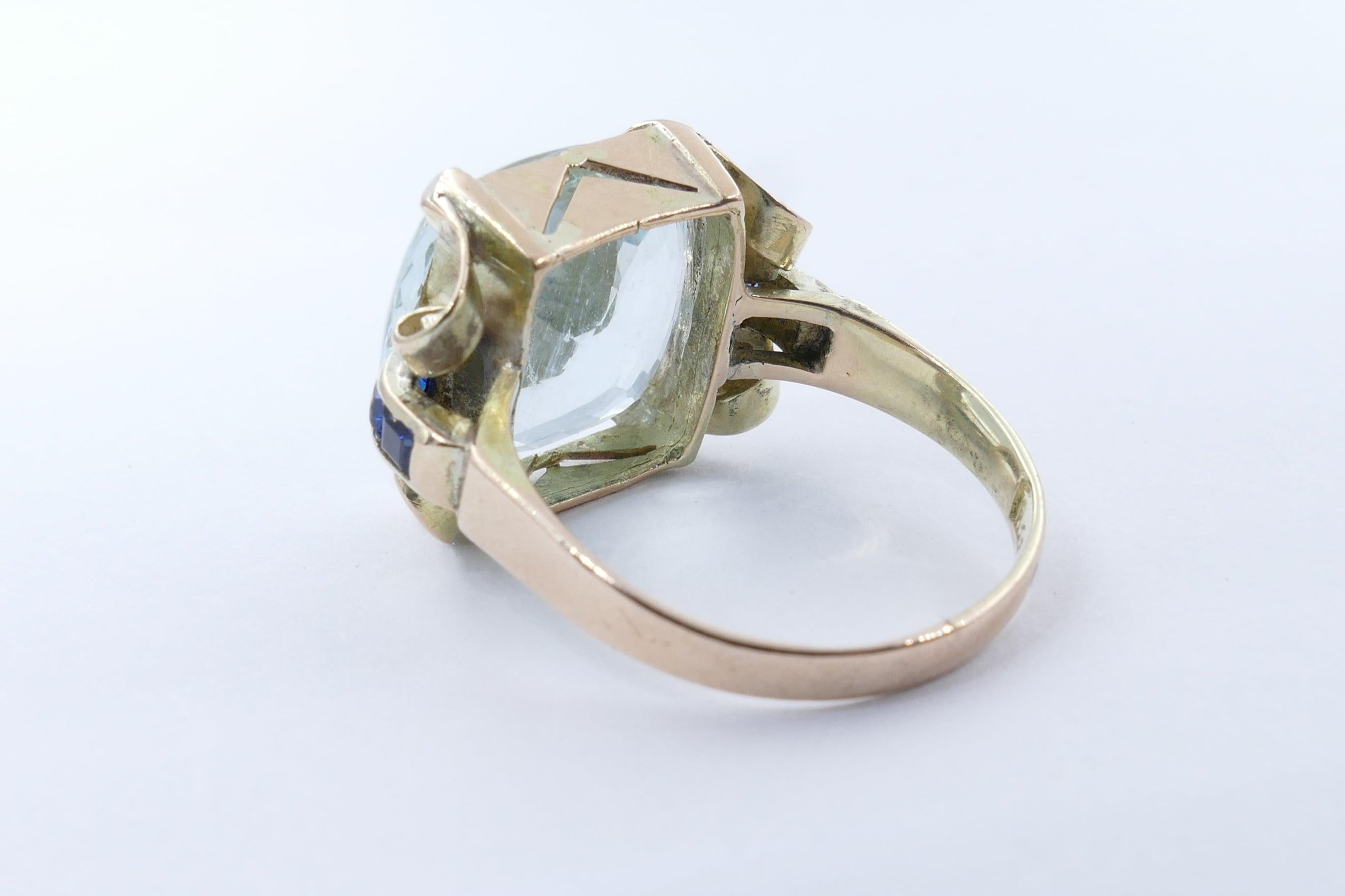 One large light greenish/blue Aquamarine 11.87 carats is the stunning centrepiece of this beautiful Ring. The stone is eye-clean, square cushion cut, 4 claw set. It is flanked by 6 bright royal blue sapphires, tone medium, clarity eye-clear &