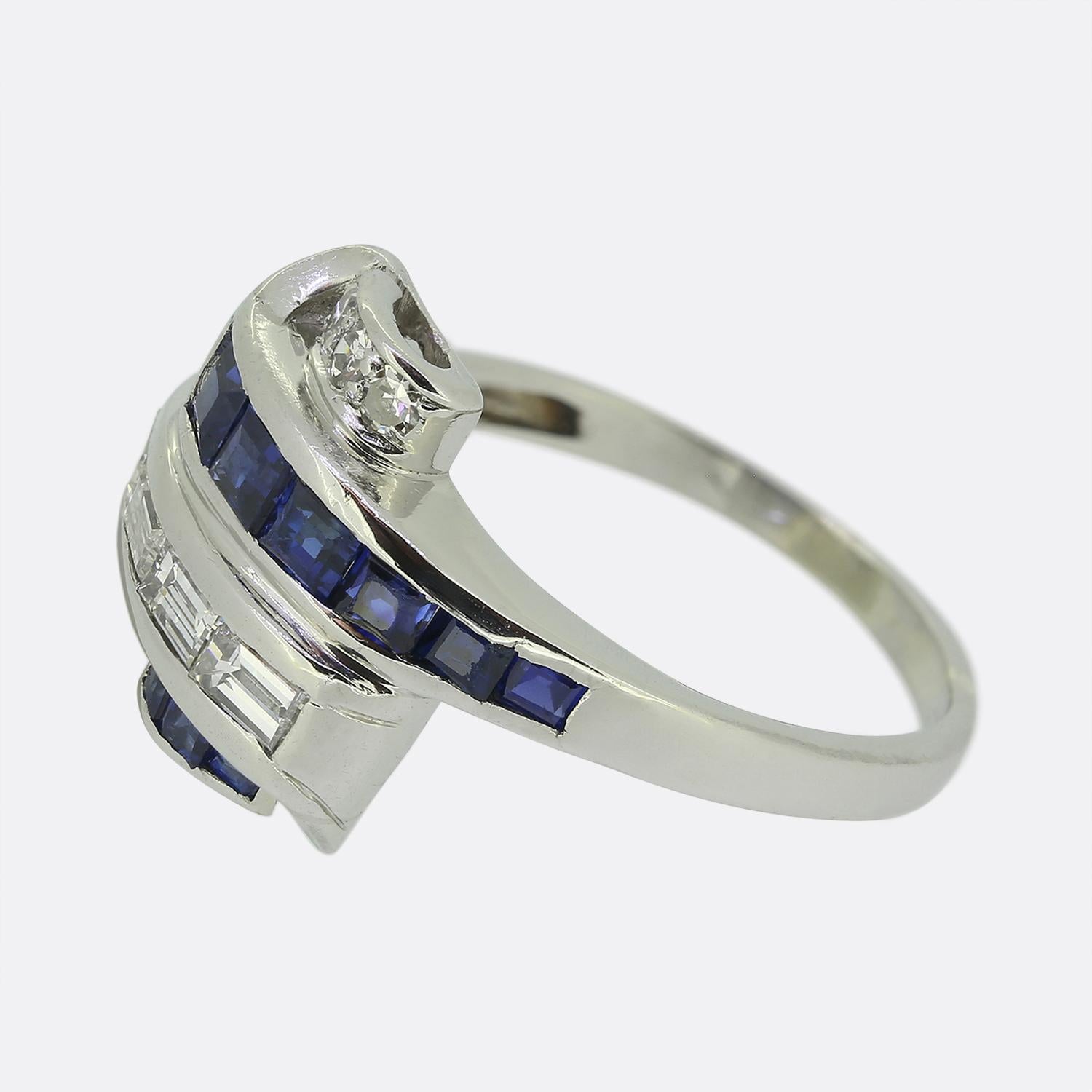 Here we have a sleek and stylish ring crafted towards the end of the Art Deco movement. This platinum piece showcases four alternating rows of sapphires and diamonds in a ribbon shaped head. A trio of eight cut diamonds sit at the top of the face