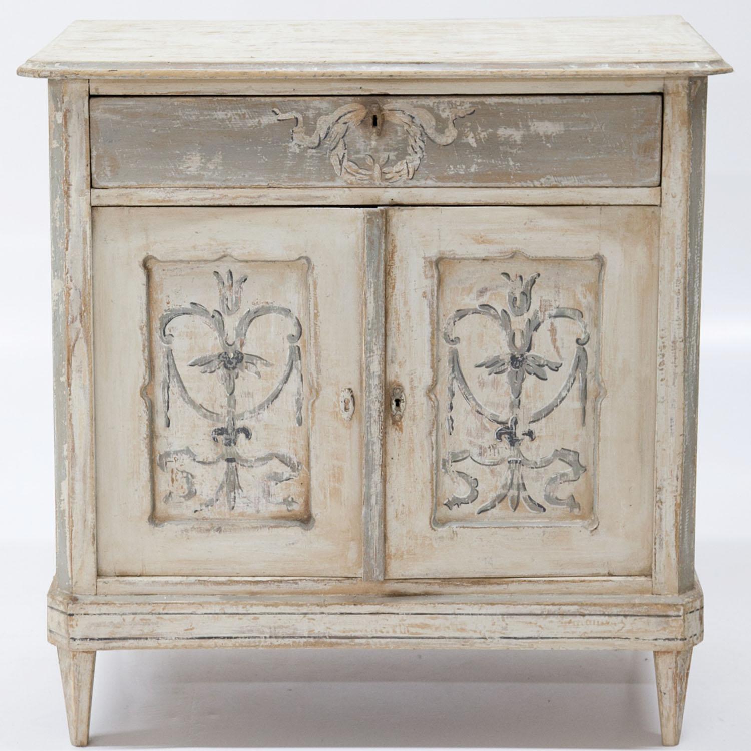 Biedermeier cabinet standing on tapered feet with two doors and one top drawer. The body with slanted corners and wavy fillings on the doors. The crème-white paint with grey decorative wreaths was redone and has a worn look to it.