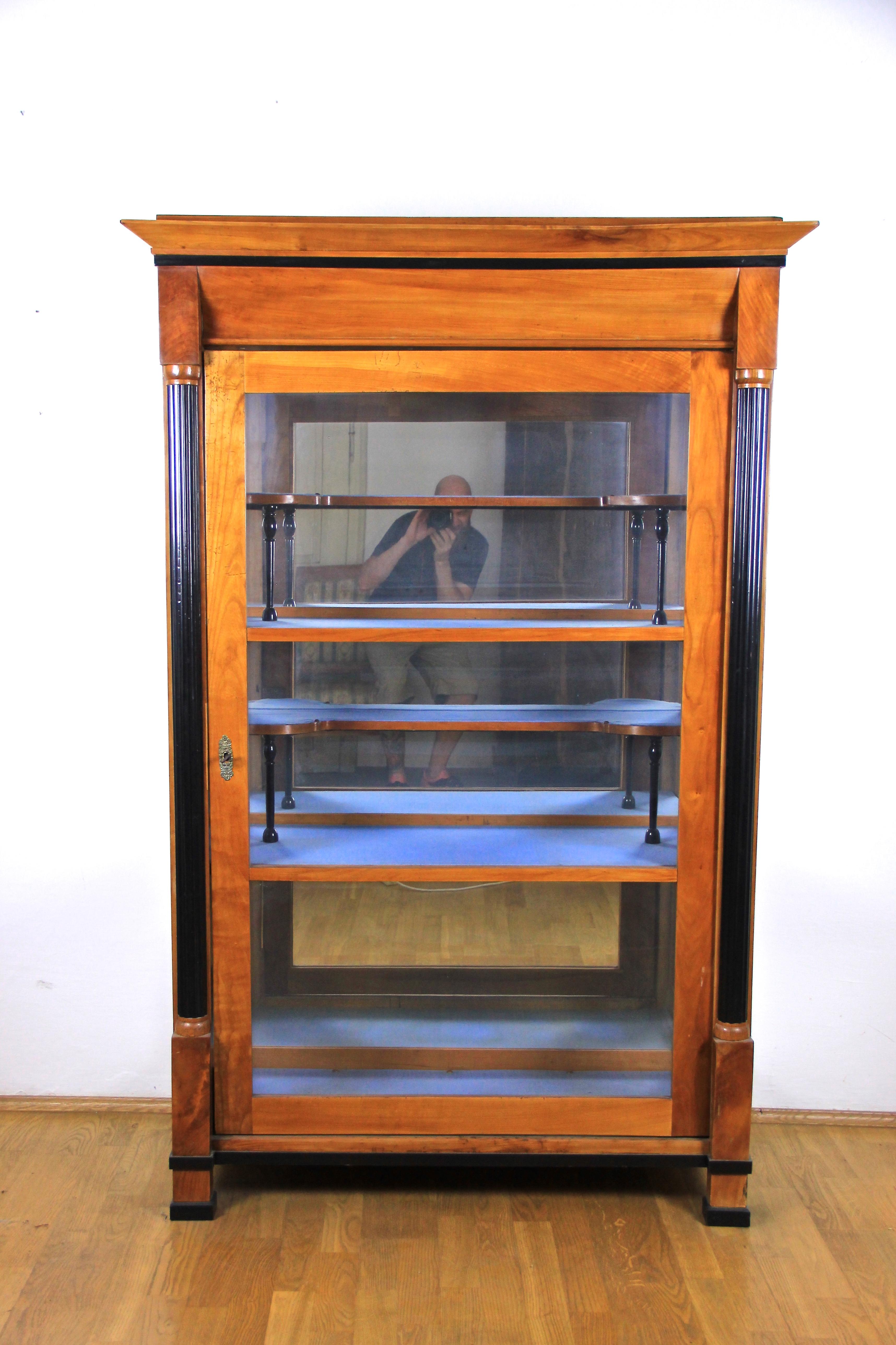 Amazing Biedermeier vitrine or display case from the very late second Biedermeier era around the end of the 19th century. Glassed on three sides, this pleasant cherry wood veneered vitrine captivates with two carved ebonized half columns. Inside you