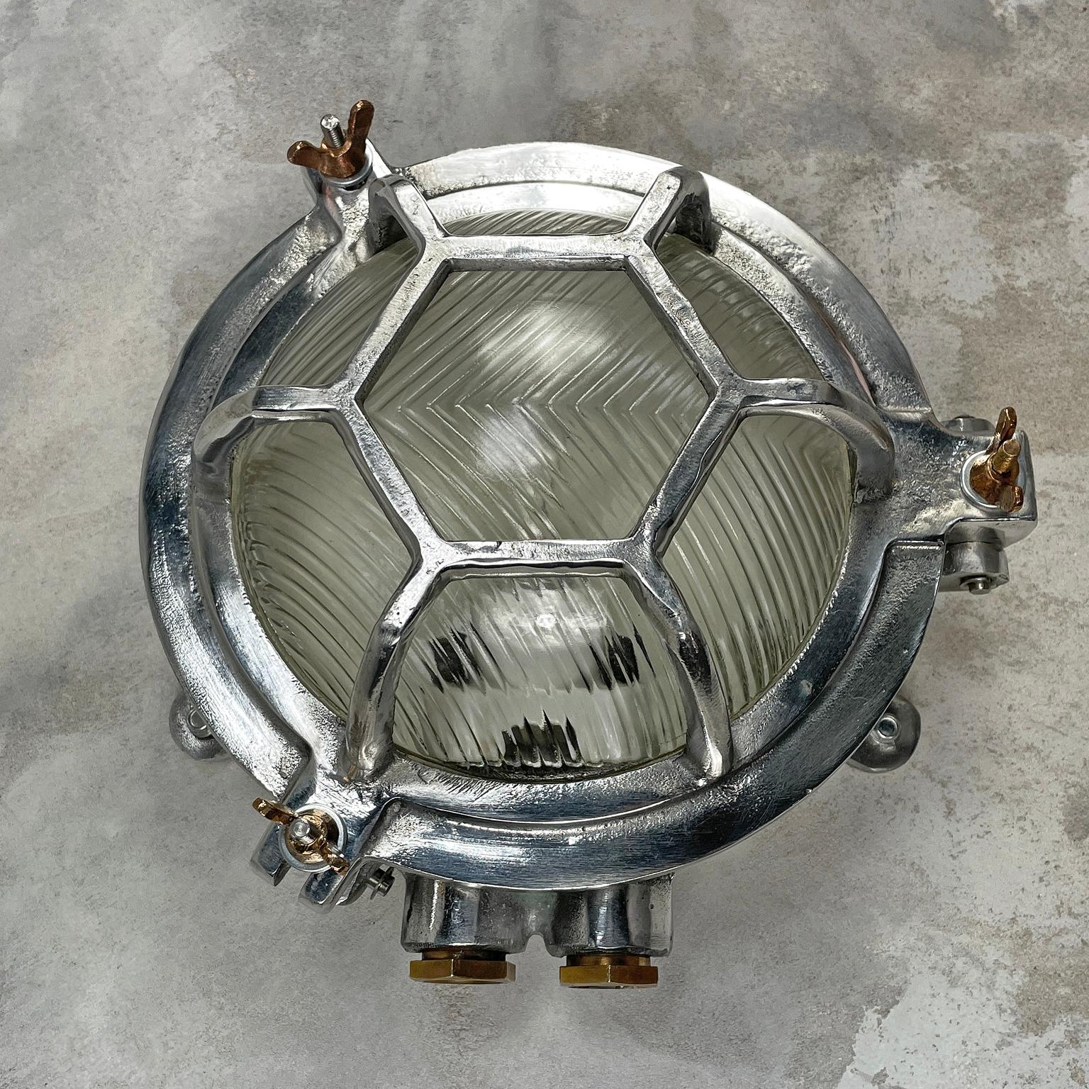 A vintage industrial aluminium outdoor circular bulkhead wall light with a hexagonal target cage and prismatic / reeded glass. 

Originally marine lighting, this type of aluminium circular bulkhead is found on ship passageways. Professionally