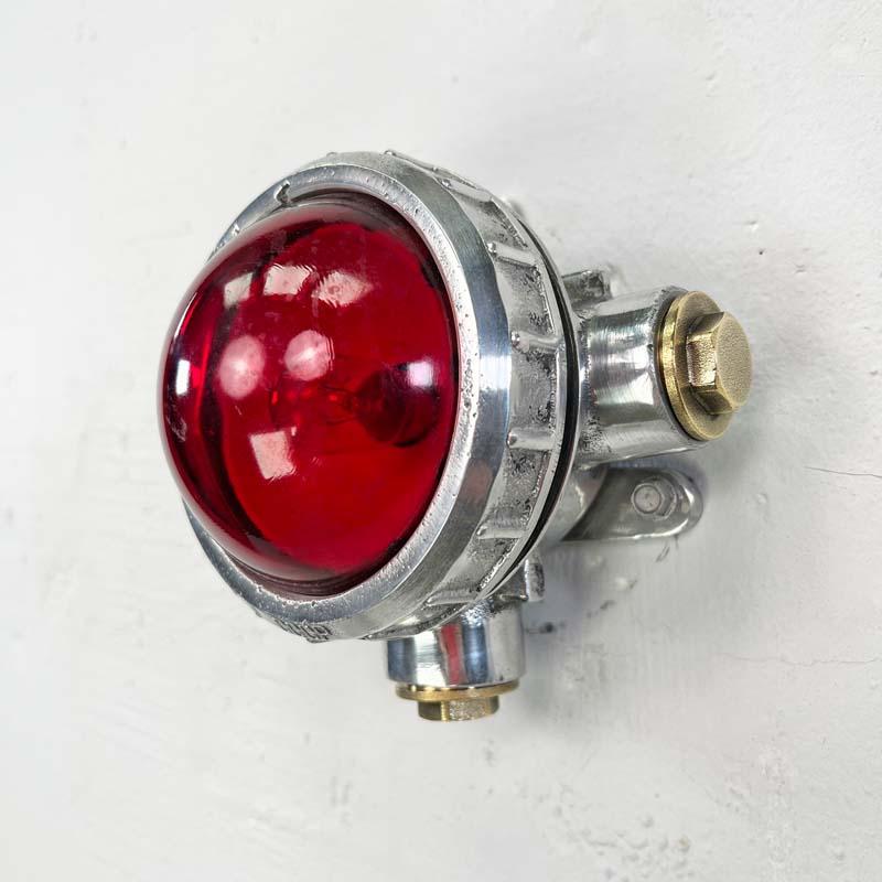 Ein kleiner industrieller Vintage-Strahler mit einer roten Glaskuppel, der als Wand- oder Deckenbeleuchtung verwendet werden kann. Verwendung mit Rohrleitungen, wenn oberflächenmontierte elektrische Kabel erforderlich sind. Dies ist eine