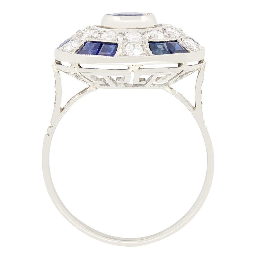 Dieser wunderschöne Clusterring aus der Zeit des Spätdekos zeigt einen intensiven blauen Saphir in der Mitte, der von einer Reihe von Diamanten und weiteren Saphiren umgeben ist. Der zentrale Edelstein ist ein 1,00 Karat großer Stein im Ovalschliff,