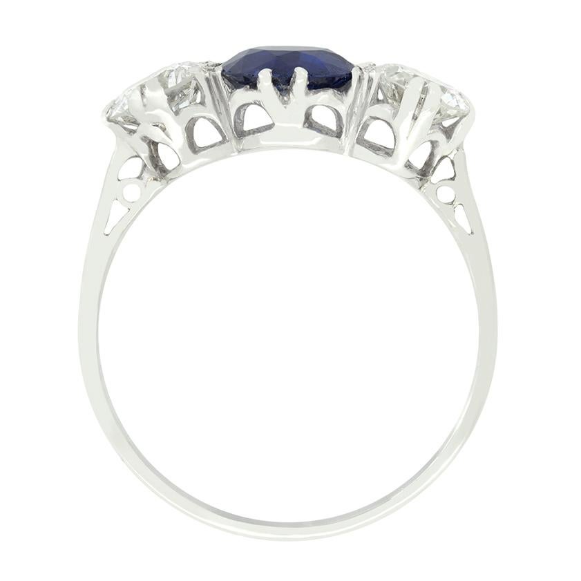 A stunning natural blue sapphire is flanked by transitional cut diamonds in this Late Deco trilogy ring. The sapphire is a 1.00 carat round cut stone with no signs of heating. The diamonds either side weigh 0.40 carat a piece, and match in quality
