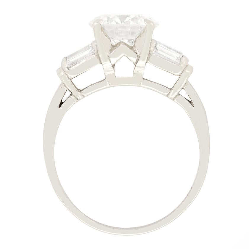 A beautiful 1.80 carat, transitional cut diamond sits central to this stunning Late Deco solitaire ring. The diamond has been certified as I in colour and SI1 in clarity. Flanking the central stone, three baguette cut diamonds are set vertically on